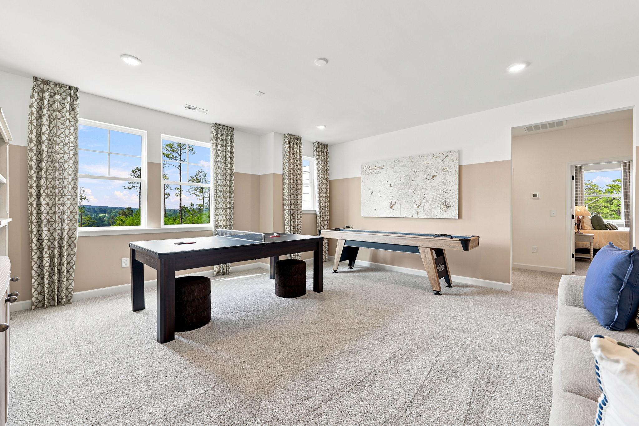 Spacious game room at Montrose in Aberdeen, NC by Davidson Homes featuring a ping pong table, shuffleboard, and lounge area.