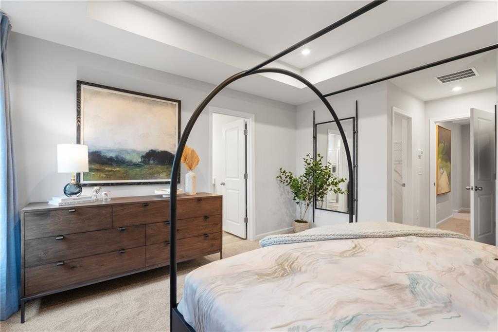 Elegant master bedroom with arched canopy bed, wooden dresser, and abstract artwork in Davidson Homes The Wilmington B, Emerson, GA