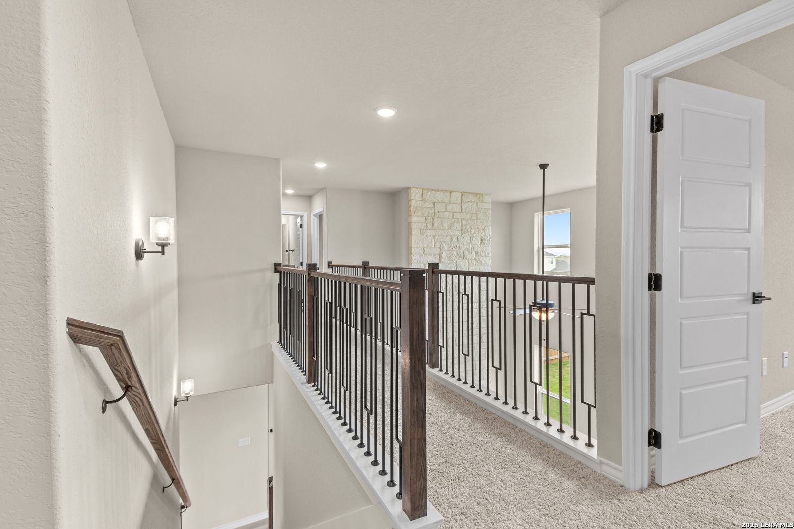 Second-floor landing with elegant metal railing and views of stone fireplace in The Danbury H, Reserve at Potranco Oaks.