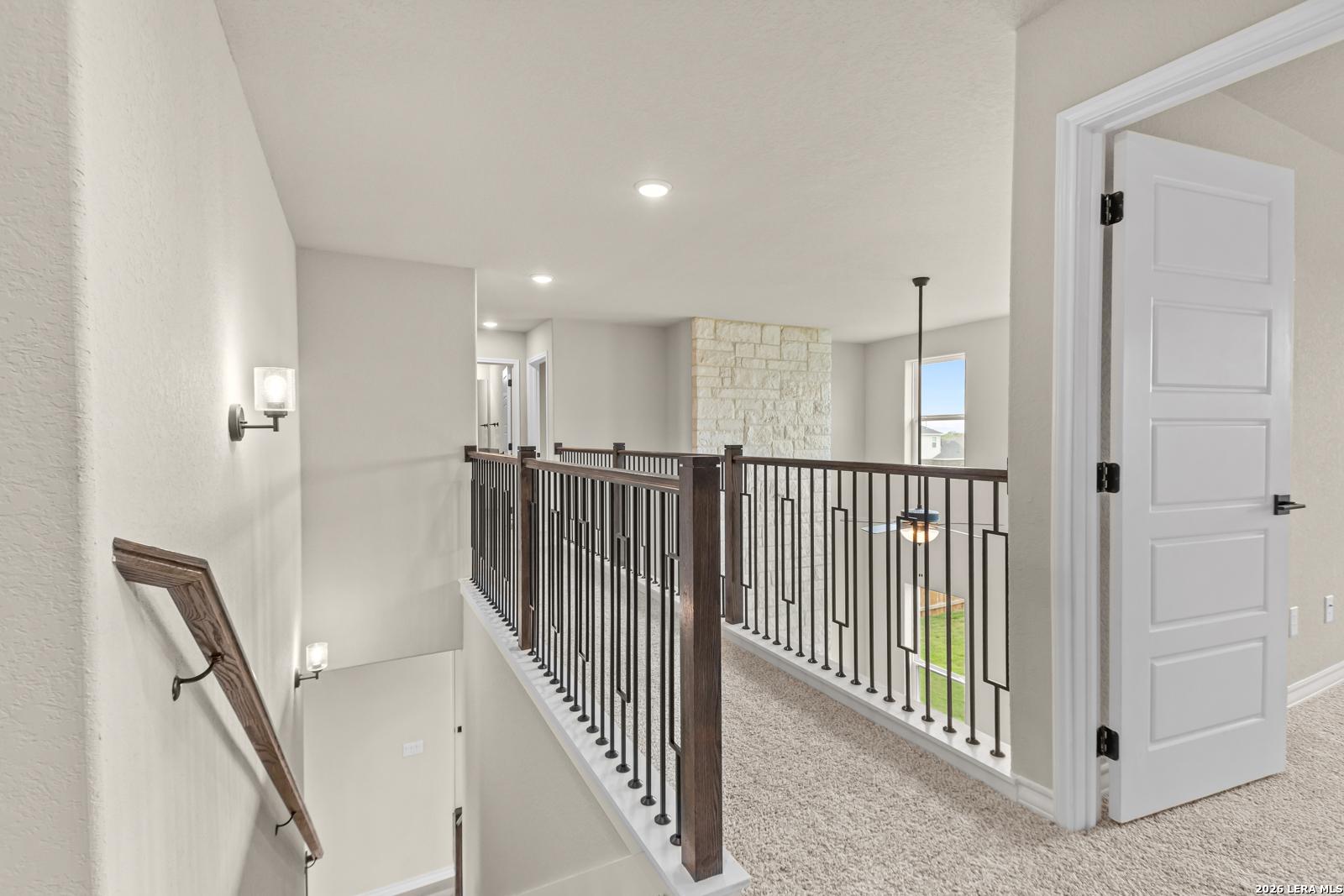 Second-floor landing with elegant metal railing and views of stone fireplace in The Danbury H, Reserve at Potranco Oaks.