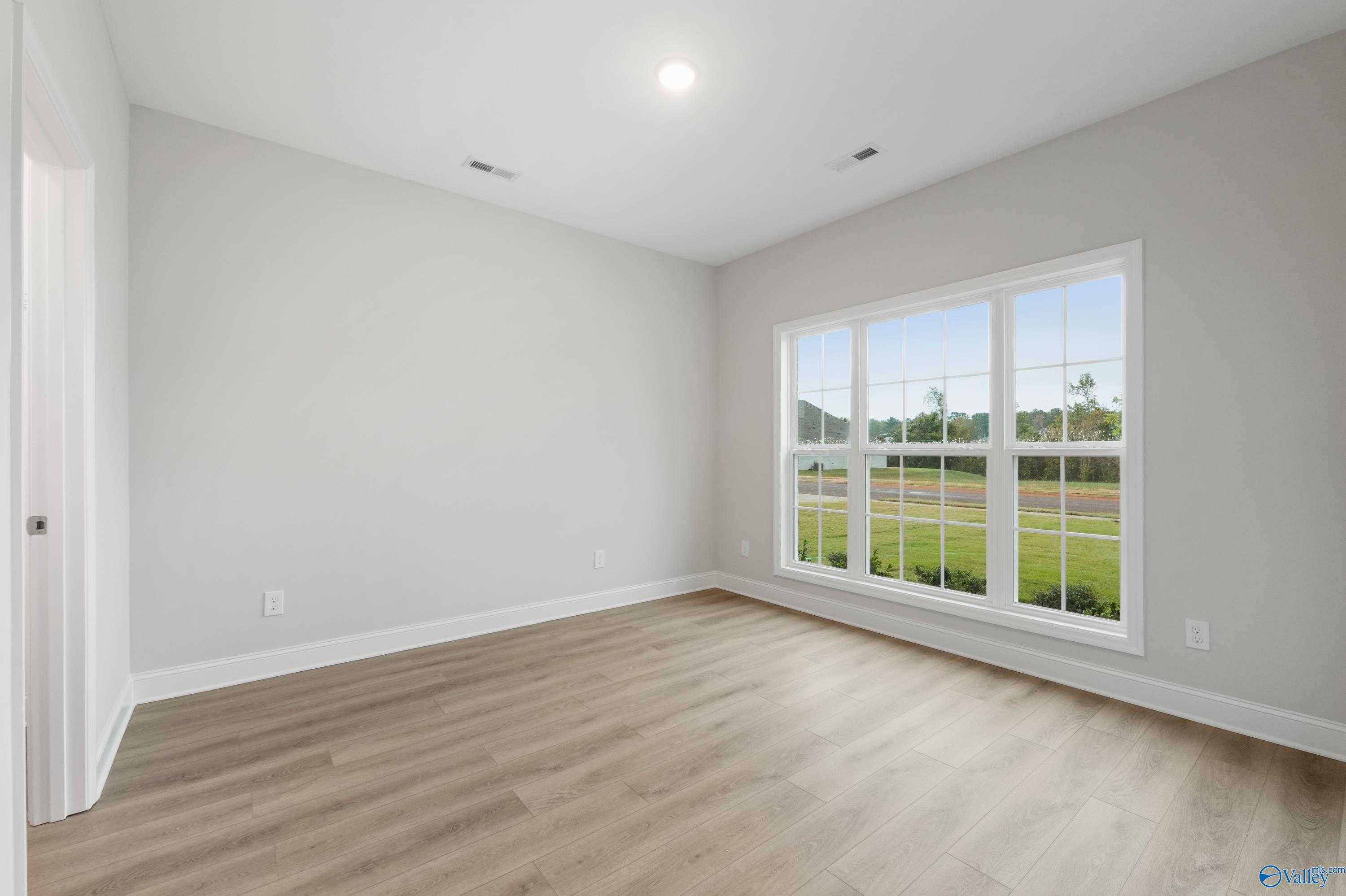 Bright empty bedroom with light gray walls, LVP flooring, and large window overlooking lawn in Davidson Homes The Lanier, Harvest AL