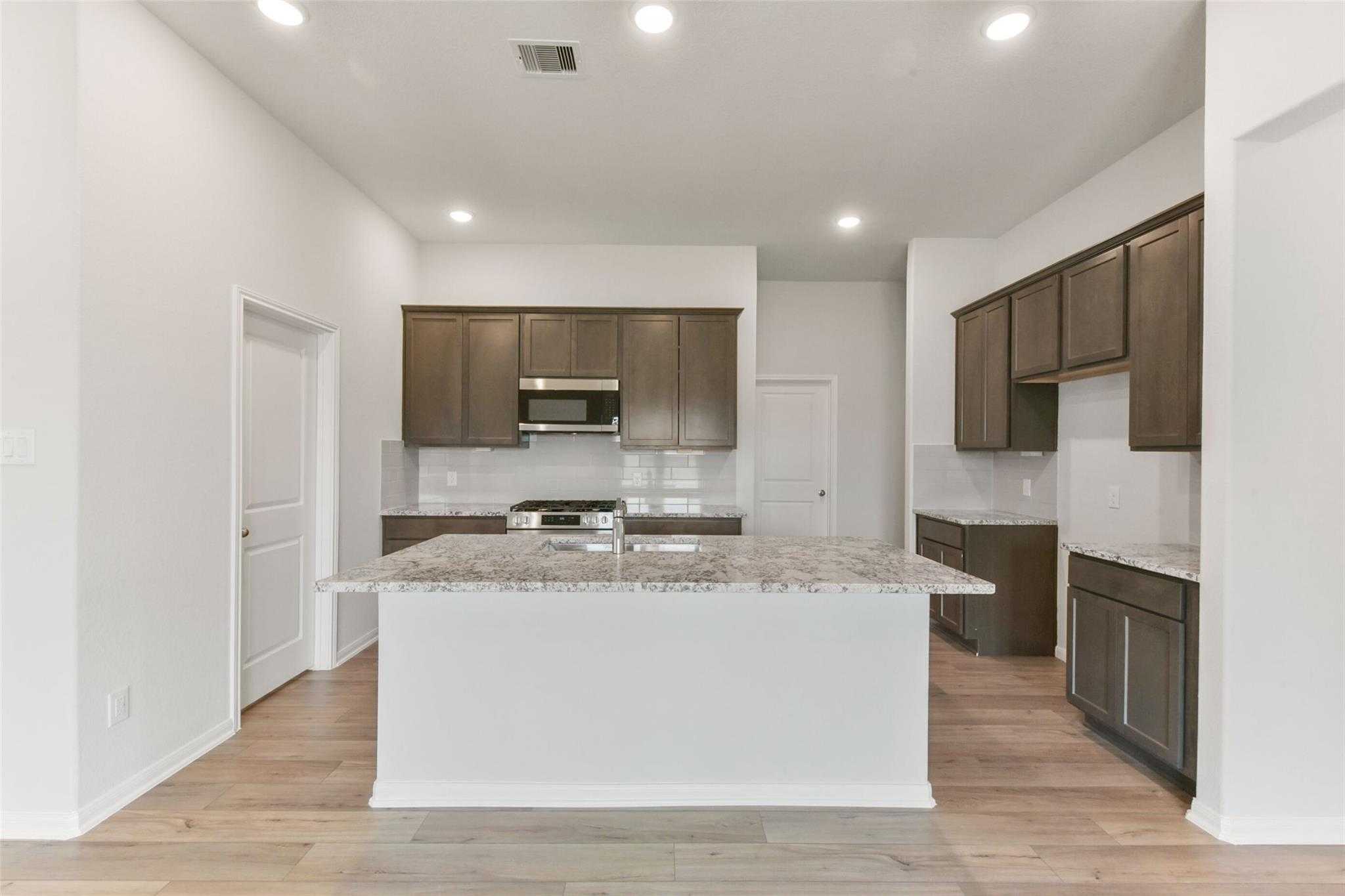 Modern kitchen with shaker cabinets, quartz island, stainless appliances in Davidson Homes The Laguna B, Magnolia TX