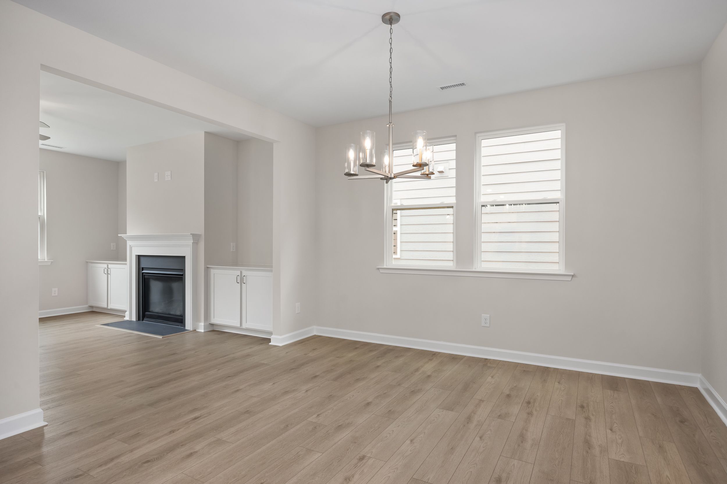 Spacious family room in The Beech A home design featuring gas fireplace, modern chandelier, hardwood floors, and large windows