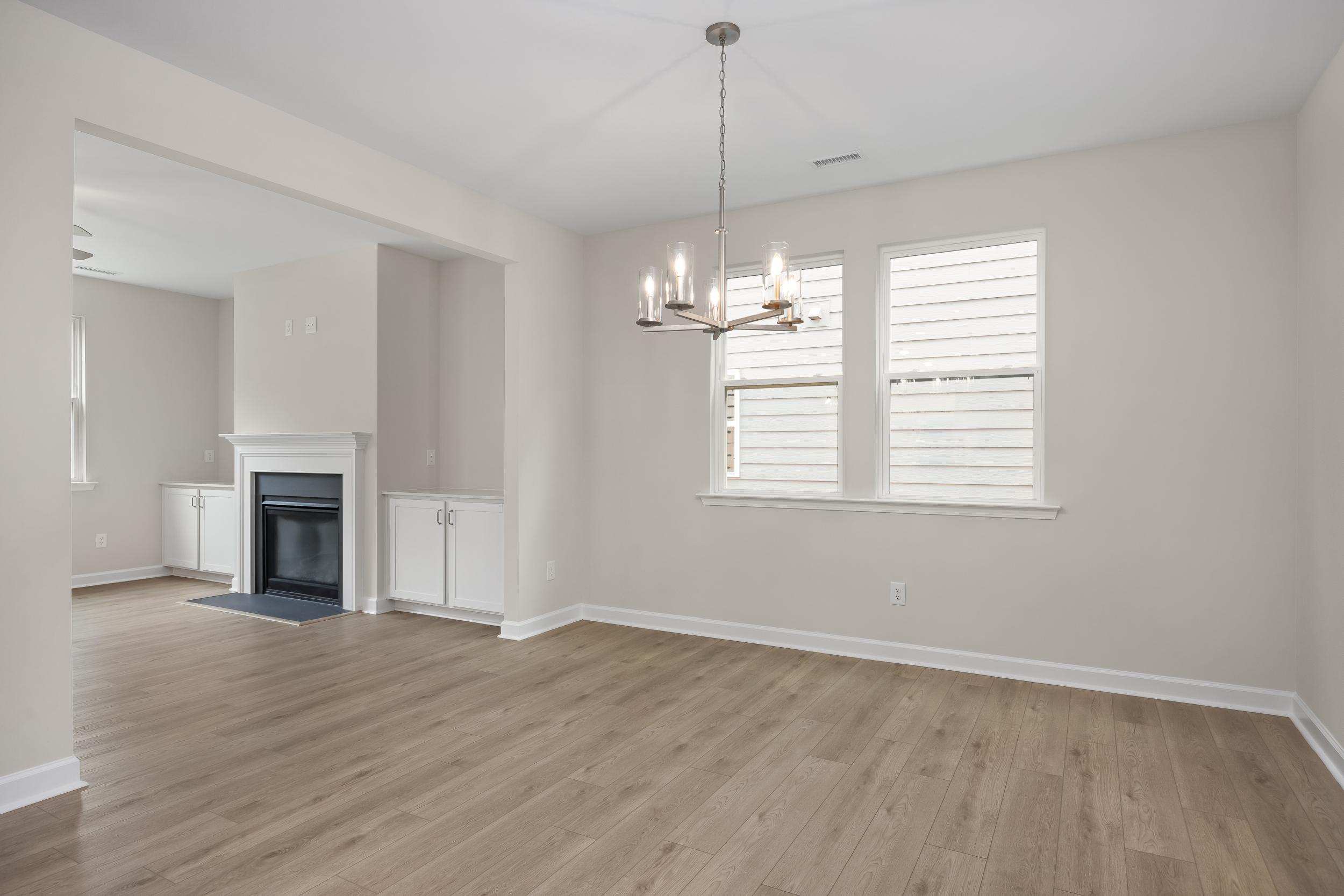 Spacious family room in The Beech A home design featuring gas fireplace, modern chandelier, hardwood floors, and large windows