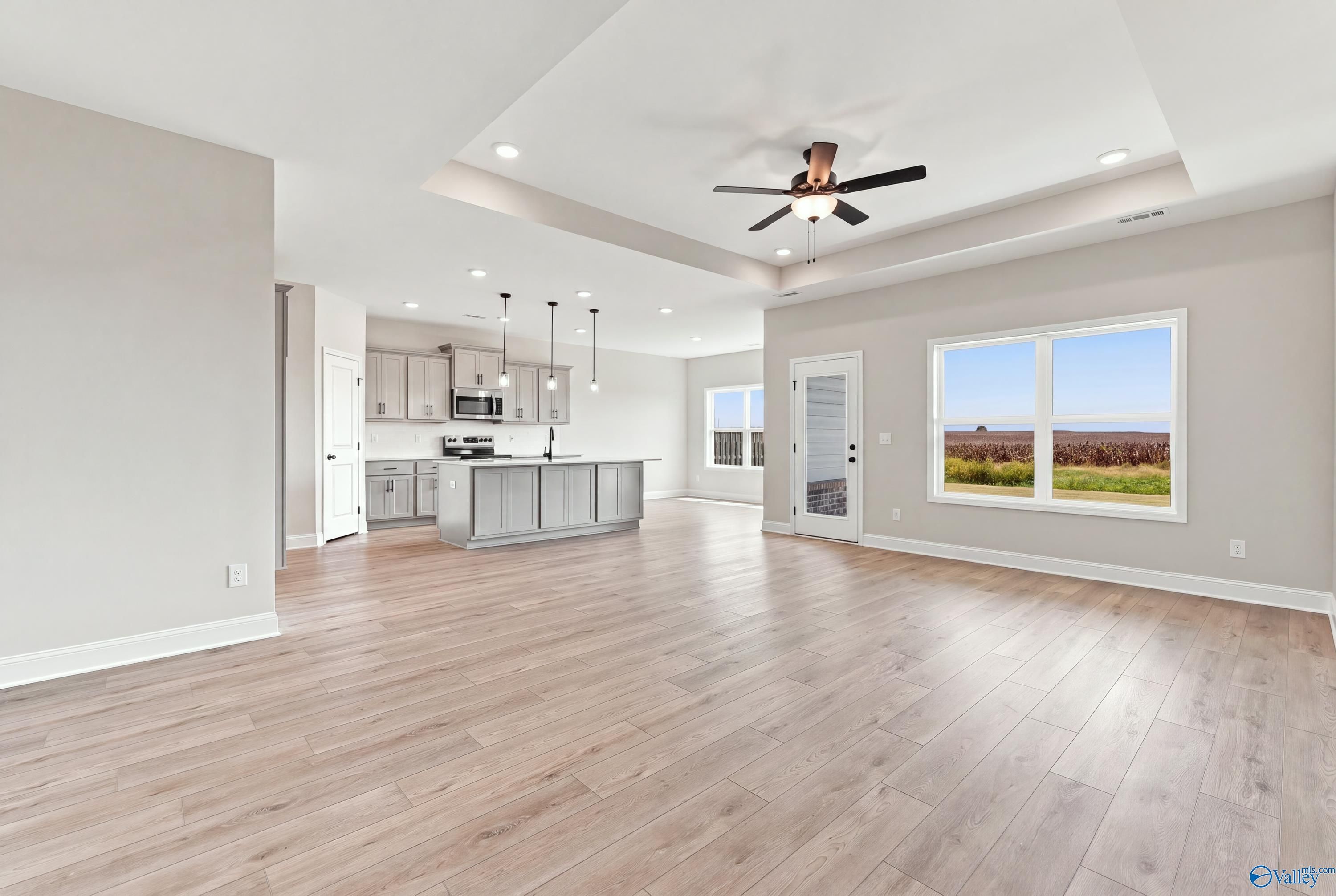 Open-concept living area with luxury vinyl plank flooring, tray ceiling, and gray kitchen island in Davidson Homes Montgomery D, Athens, AL