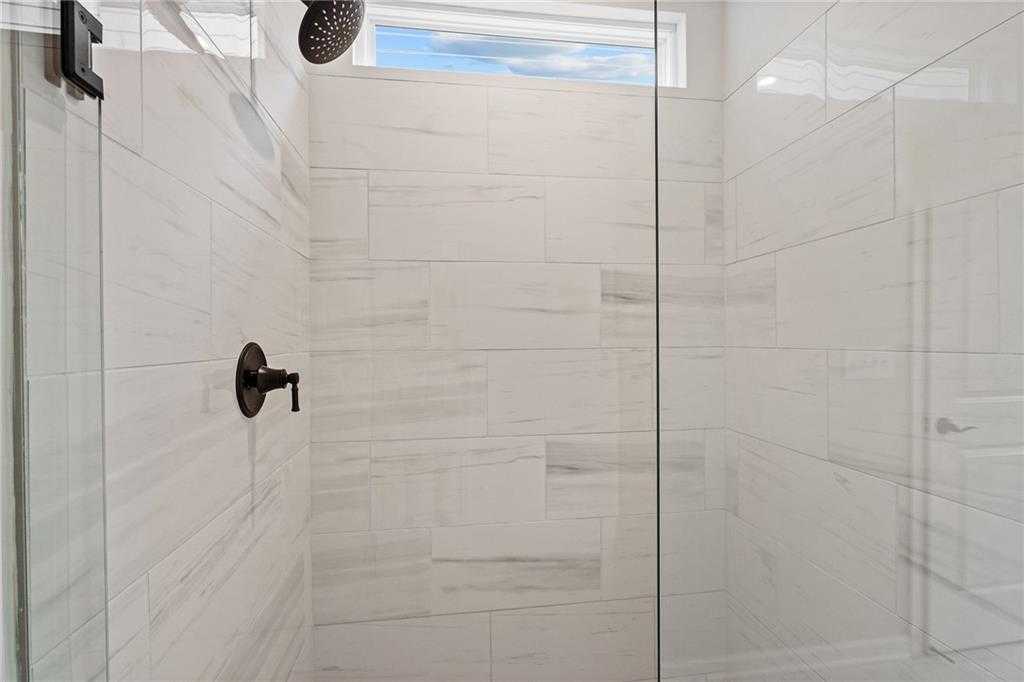 Modern walk-in shower with white subway tiles, rain showerhead, frameless glass door, and transom window in Davidson Homes The Glenwood C, Loganville, GA