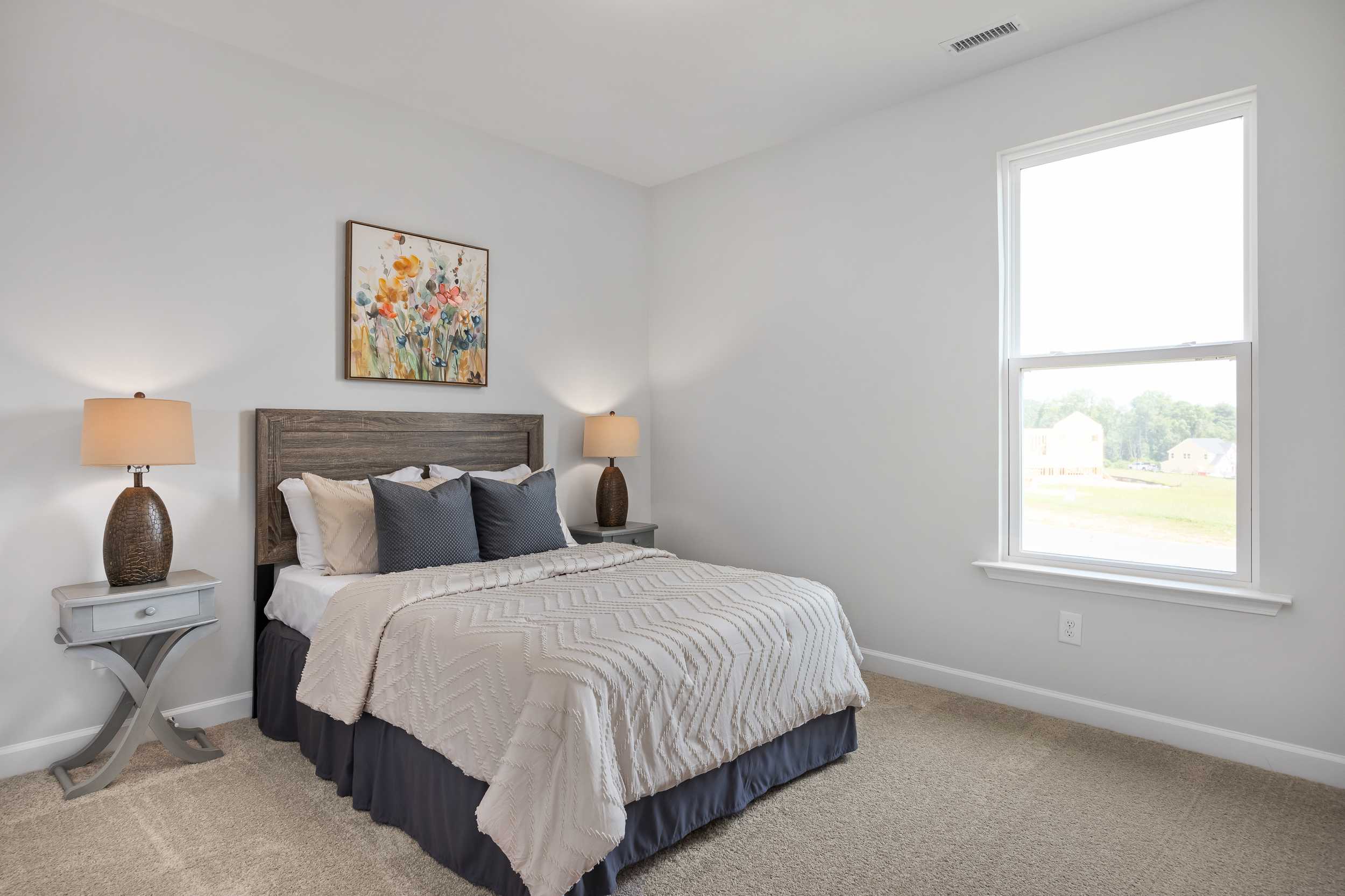 Spacious master bedroom in The Daphne C featuring neutral bed linens, wooden headboard, bedside lamps, and large window in Mooresville home