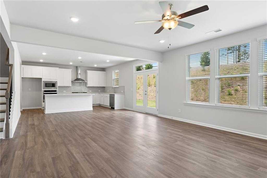 Spacious open kitchen-living area with white cabinets, stainless appliances, hardwood floors, ceiling fan, and sliding doors in Davidson Homes Hickory B, Winder GA