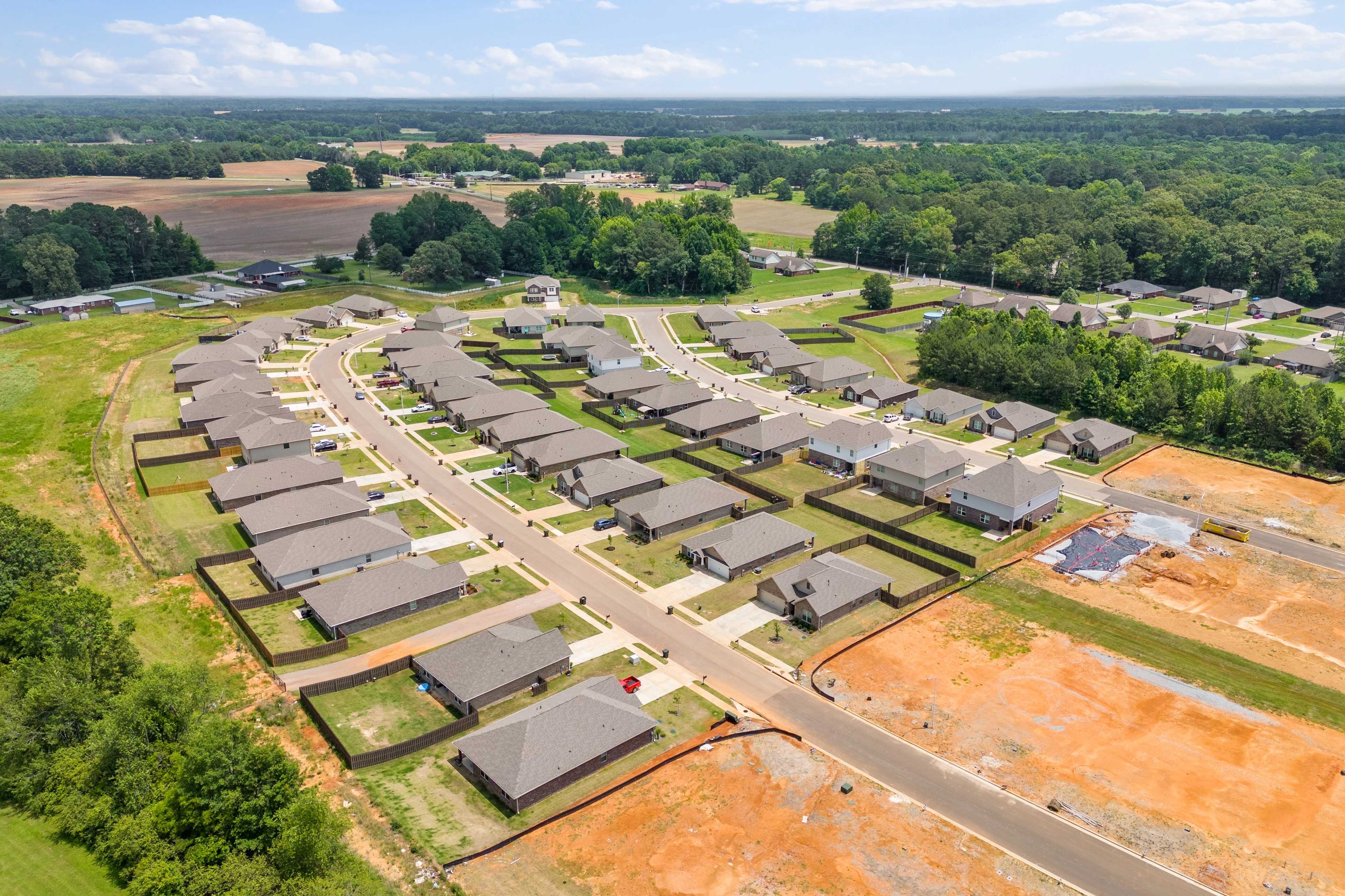 Aerial view of new homes under construction in Durham Farms, Harvest Alabama, with green fields and wooded surroundings