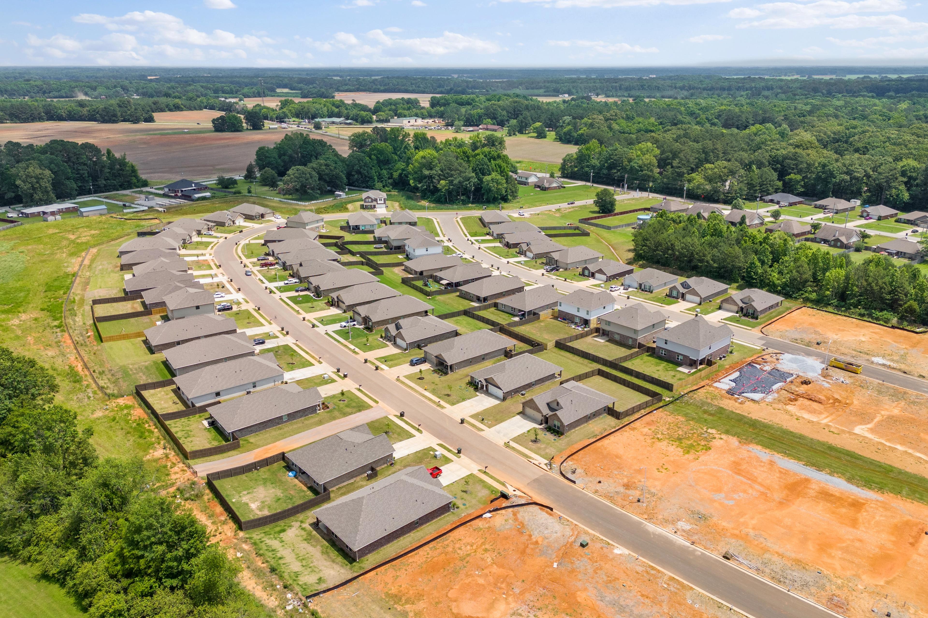 Aerial view of new homes under construction in Durham Farms, Harvest Alabama, with green fields and wooded surroundings