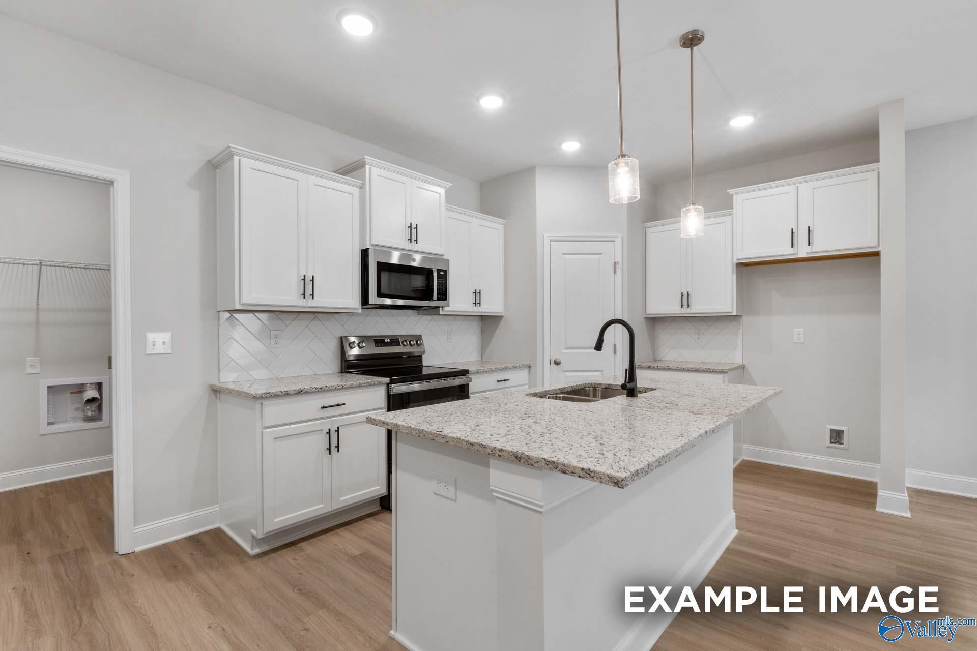 Modern kitchen with white cabinets, granite island, and stainless appliances in The Camilla B floor plan at Cain Park.