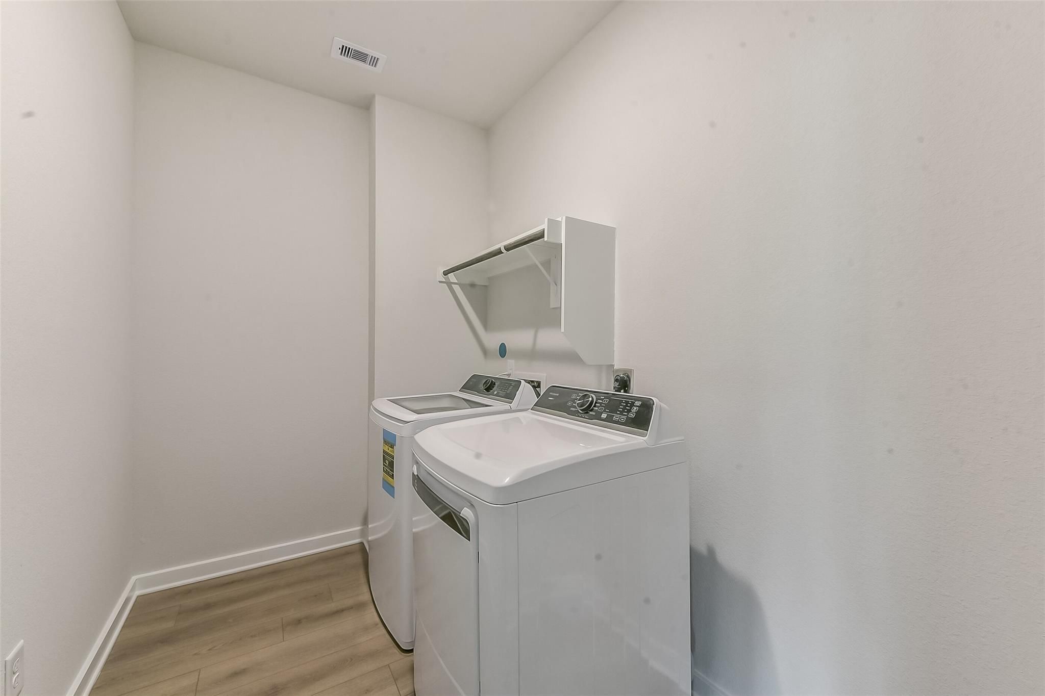 Modern laundry room with white front-load washer, dryer, and overhead cabinet on laminate flooring in Davidson Homes Everett C, Crosby, Texas