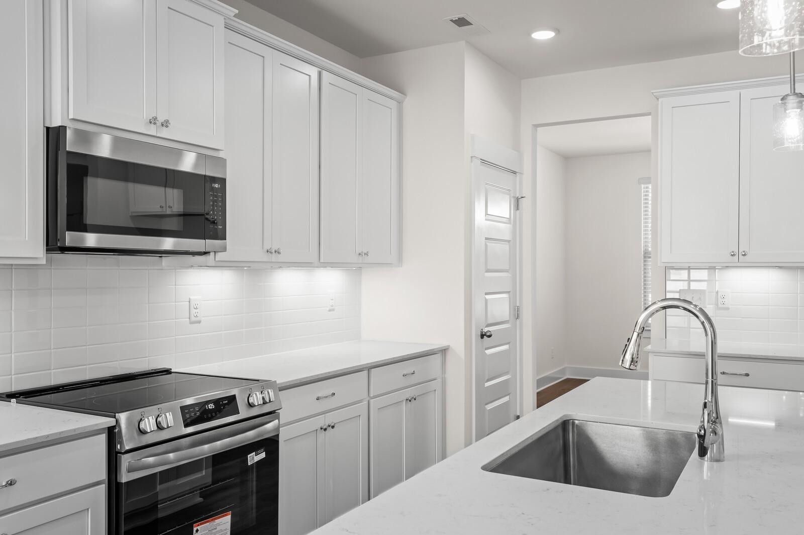 Modern kitchen with white cabinets, quartz countertops, and stainless steel appliances in The Ash A at Woods Crossing.