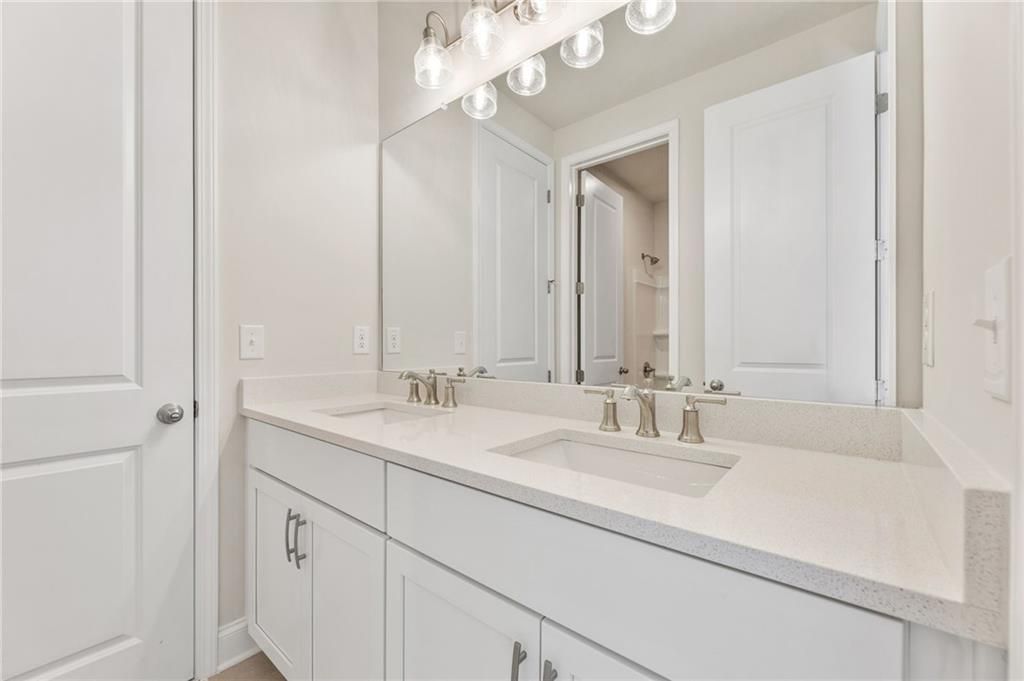 Modern double vanity bathroom with white shaker cabinets, quartz counters, and large mirror in The Danbury E home, Buford, GA