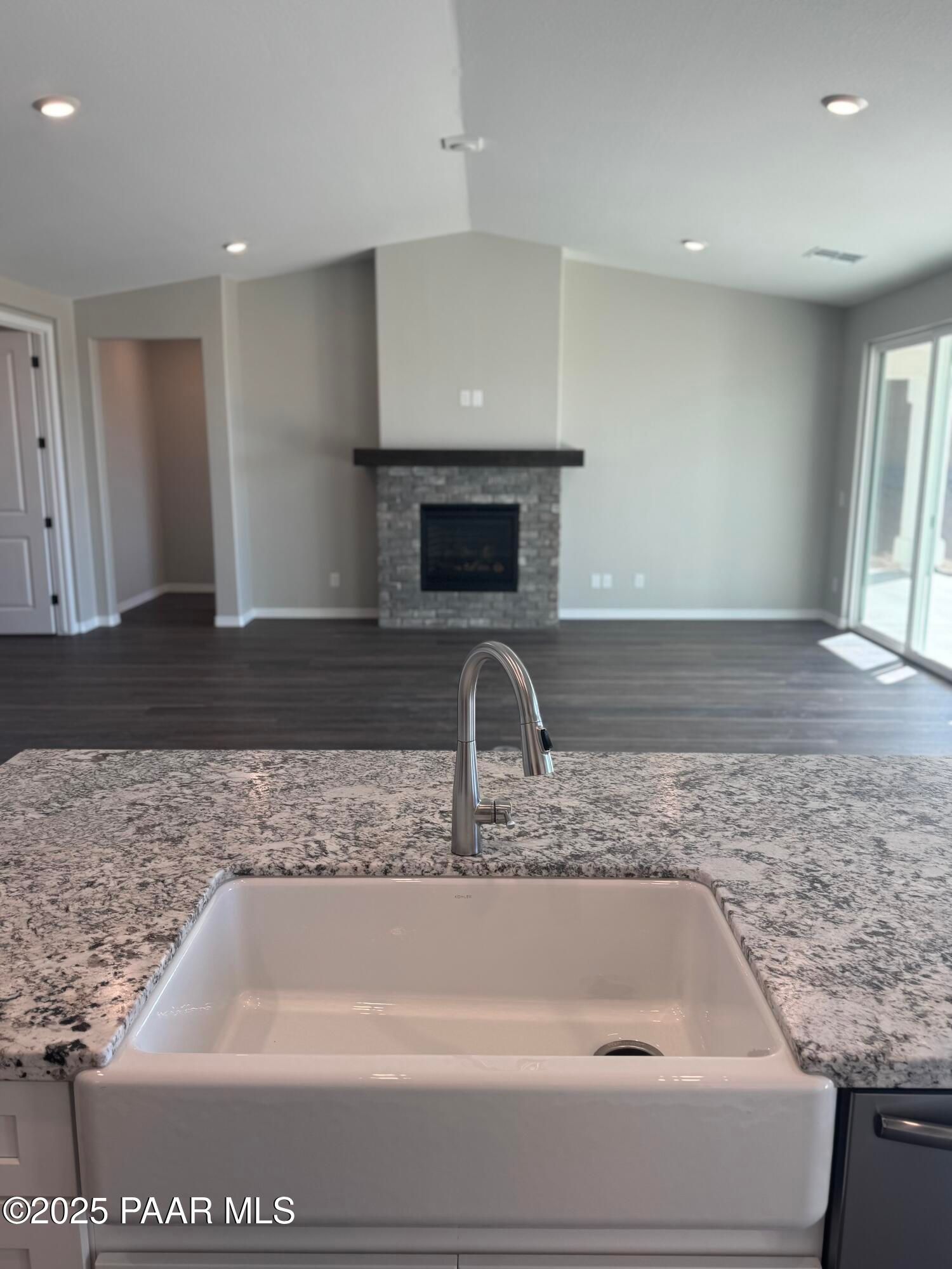 Open-concept kitchen island with quartz countertop, farmhouse sink, and stone fireplace in The Monarch E, Westwood, Prescott, Arizona