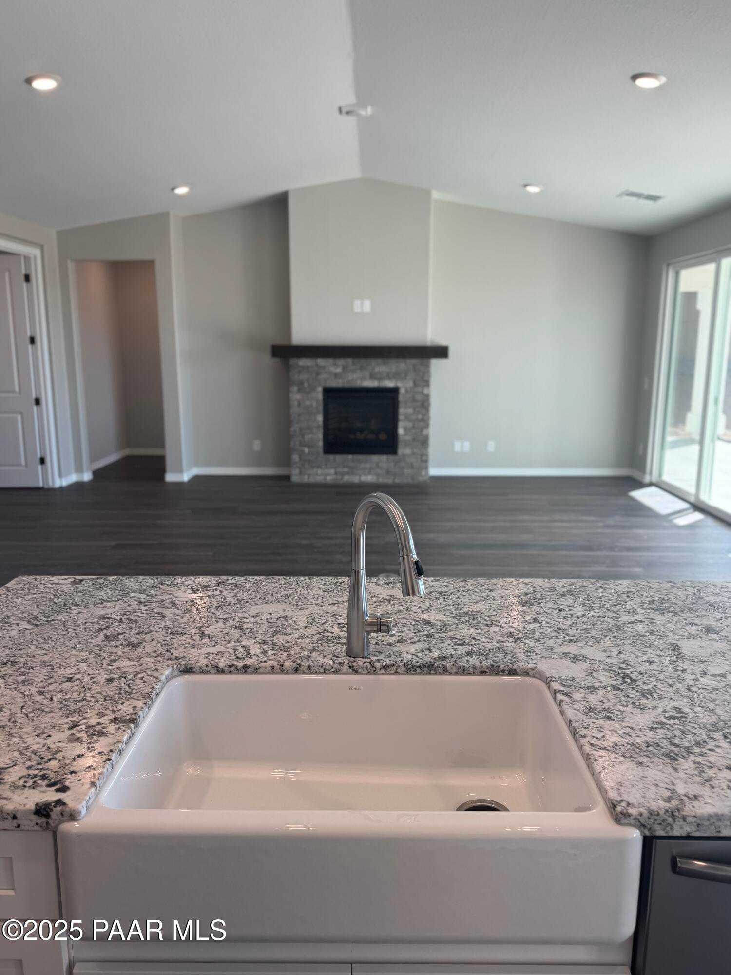 Open-concept kitchen island with quartz countertop, farmhouse sink, and stone fireplace in The Monarch E, Westwood, Prescott, Arizona