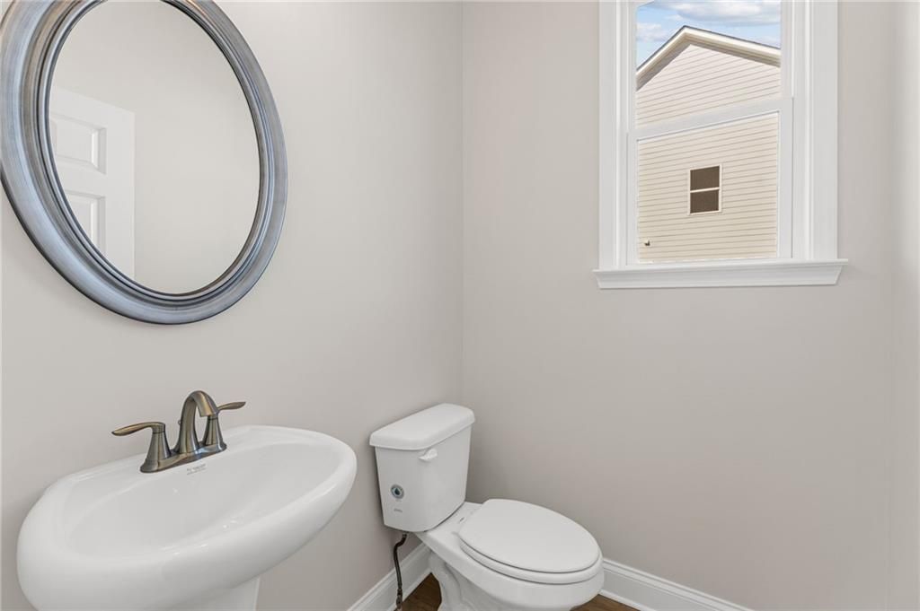 Elegant powder room with white pedestal sink, round mirror, and window view in Davidson Homes The Willow B, Hoschton, Georgia
