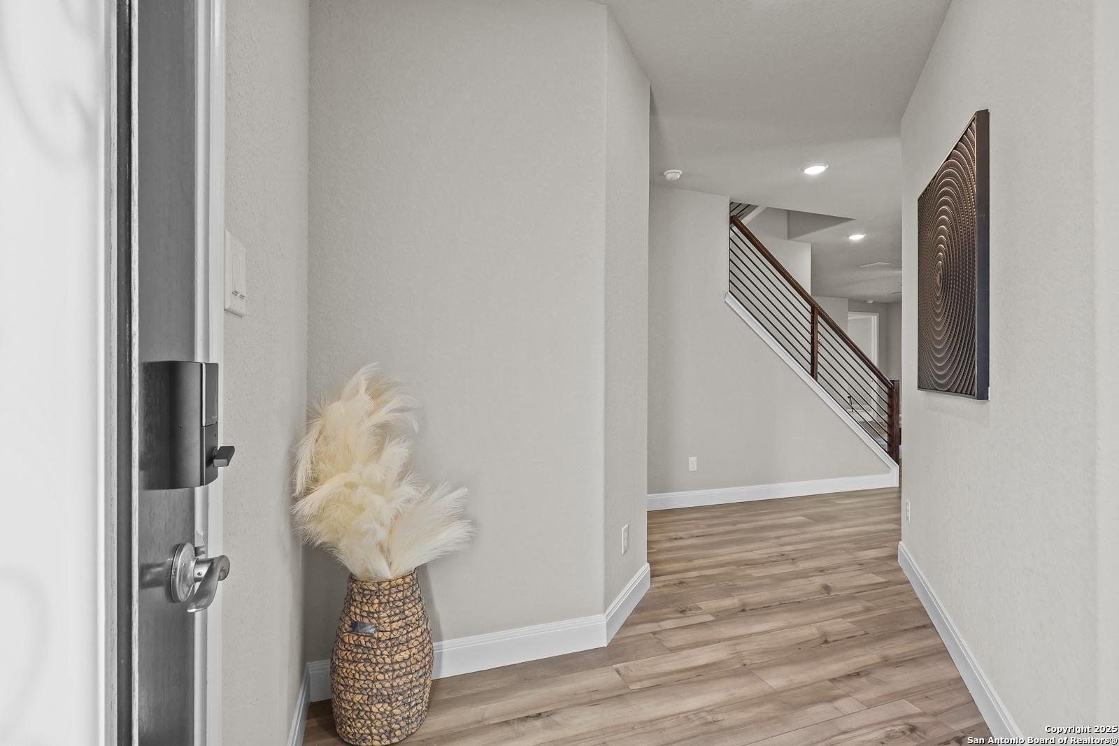Welcoming entry foyer with hardwood floors, cable staircase, pampas grass decor, and abstract wall art in Davidson Homes The Jennings G, Castroville, Texas