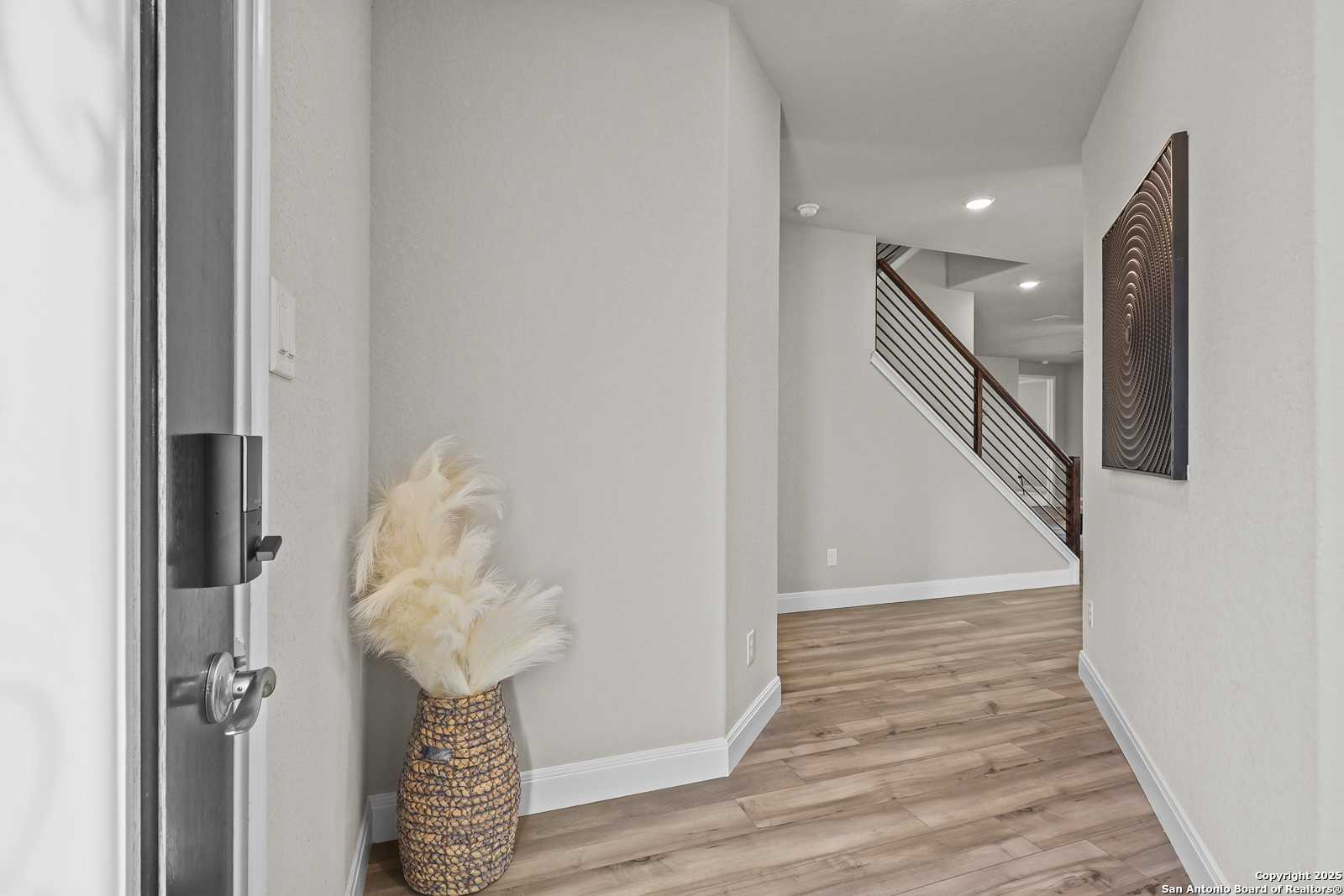 Welcoming entry foyer with hardwood floors, cable staircase, pampas grass decor, and abstract wall art in Davidson Homes The Jennings G, Castroville, Texas