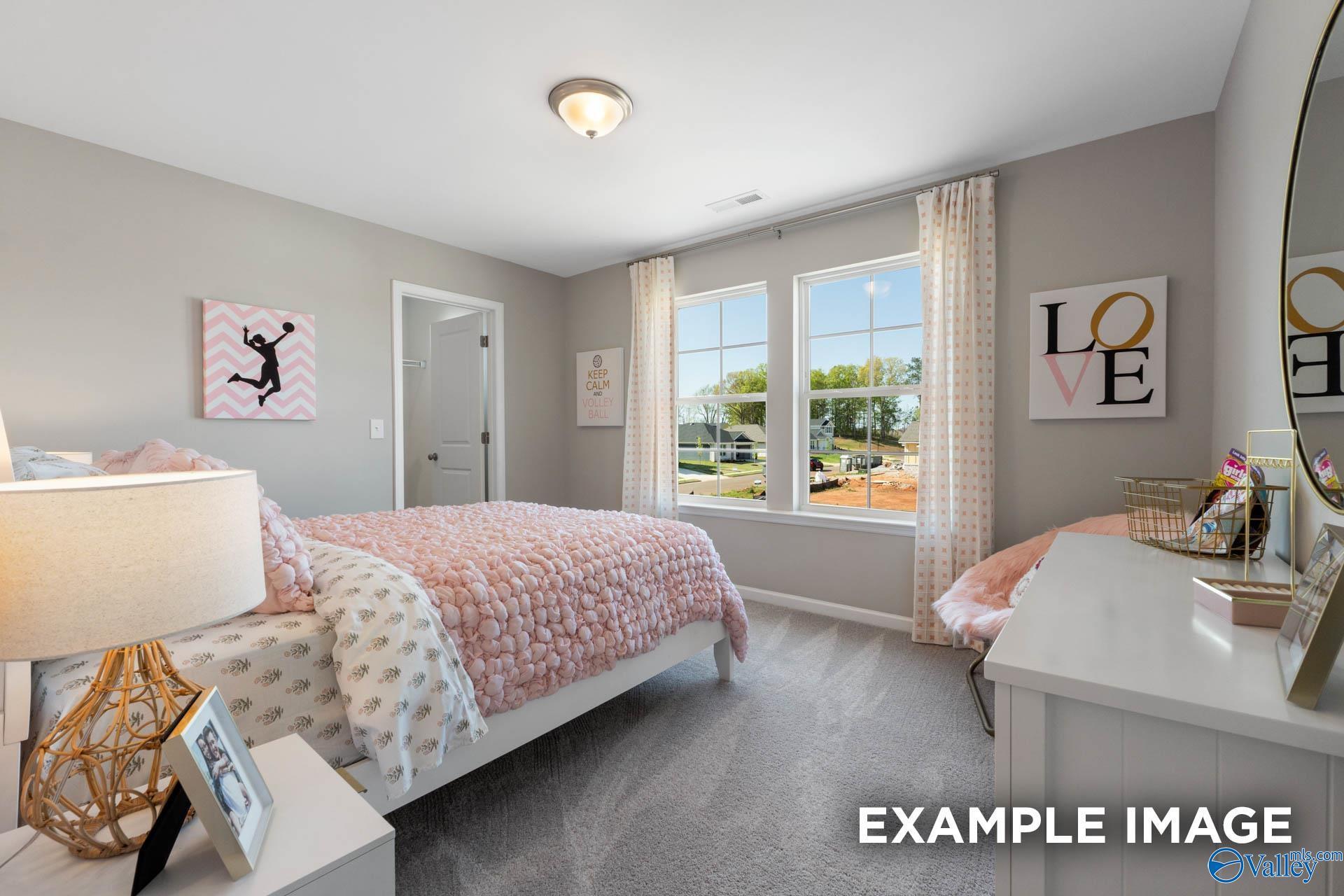 Charming secondary bedroom with pink polka-dot bedding, vanity desk, and window views in Davidson Homes The Stella, Madison, Alabama