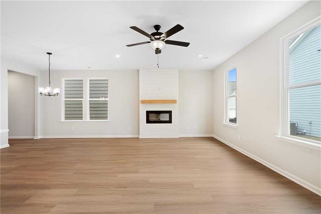 Spacious living room with gas fireplace, hardwood floors, ceiling fan, and large windows in Davidson Homes The Marion A, Kennesaw, Georgia