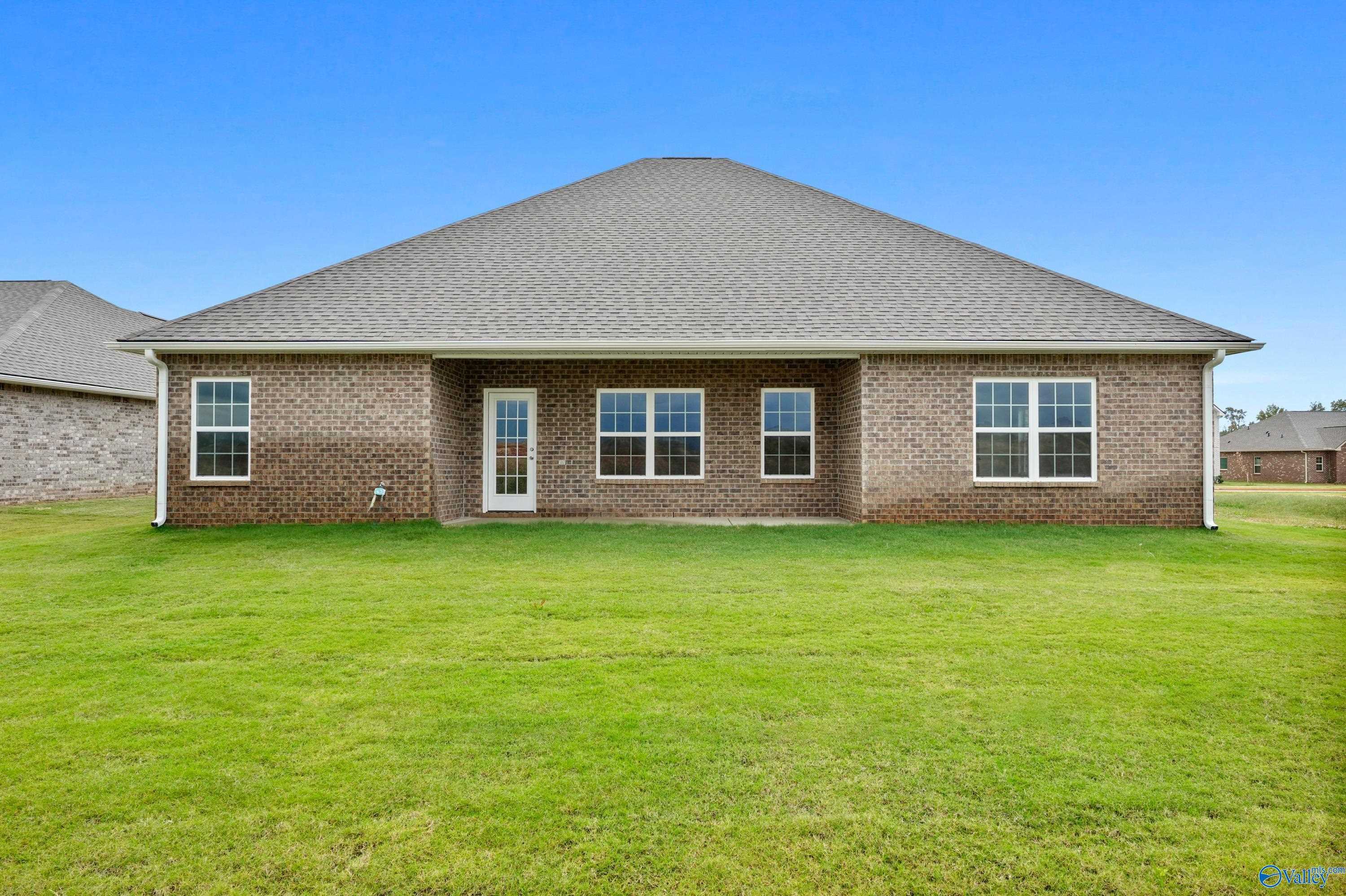 Rear view of single-story brick home with covered patio, large windows, and expansive green backyard in Creekside, Harvest, Alabama