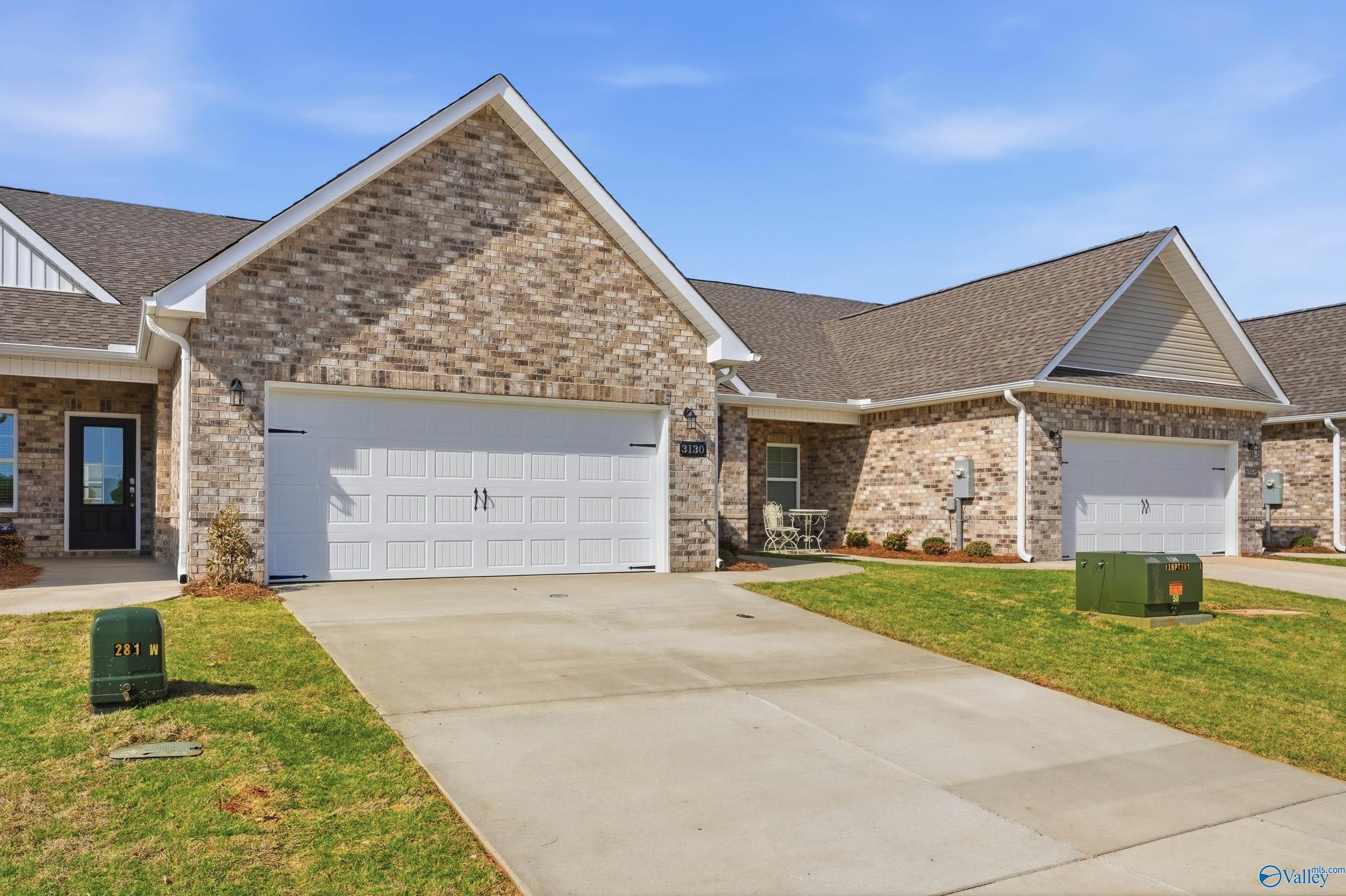 Brick ranch home with white 2-car garage doors, driveway, and lush lawn in The Retreat at Hollon Meadow, Decatur, Alabama