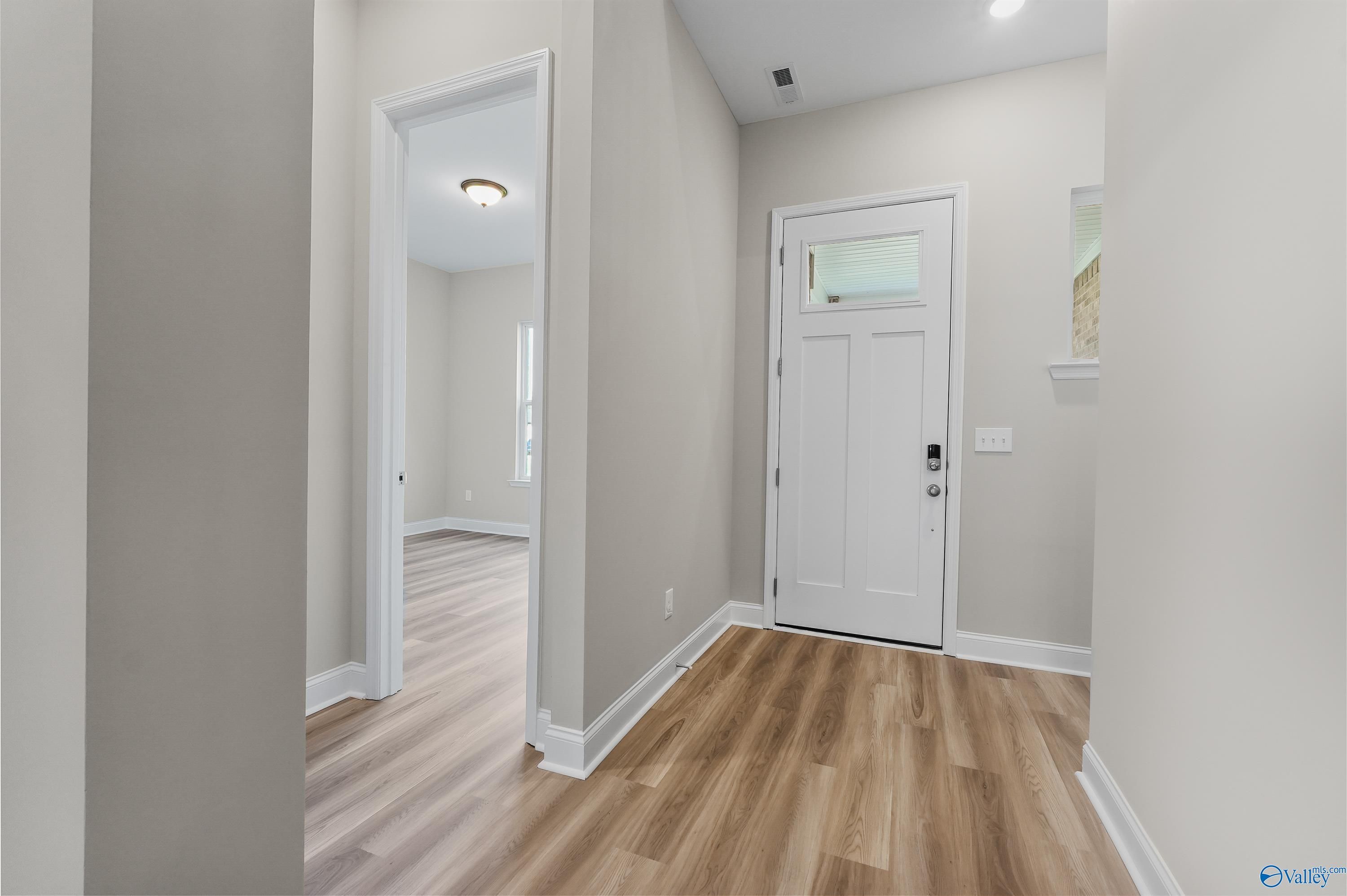 Welcoming entry foyer with light oak floors, white glass-paneled door, and neutral walls in Evermore Homes The Haven, Owens Cross Roads, AL