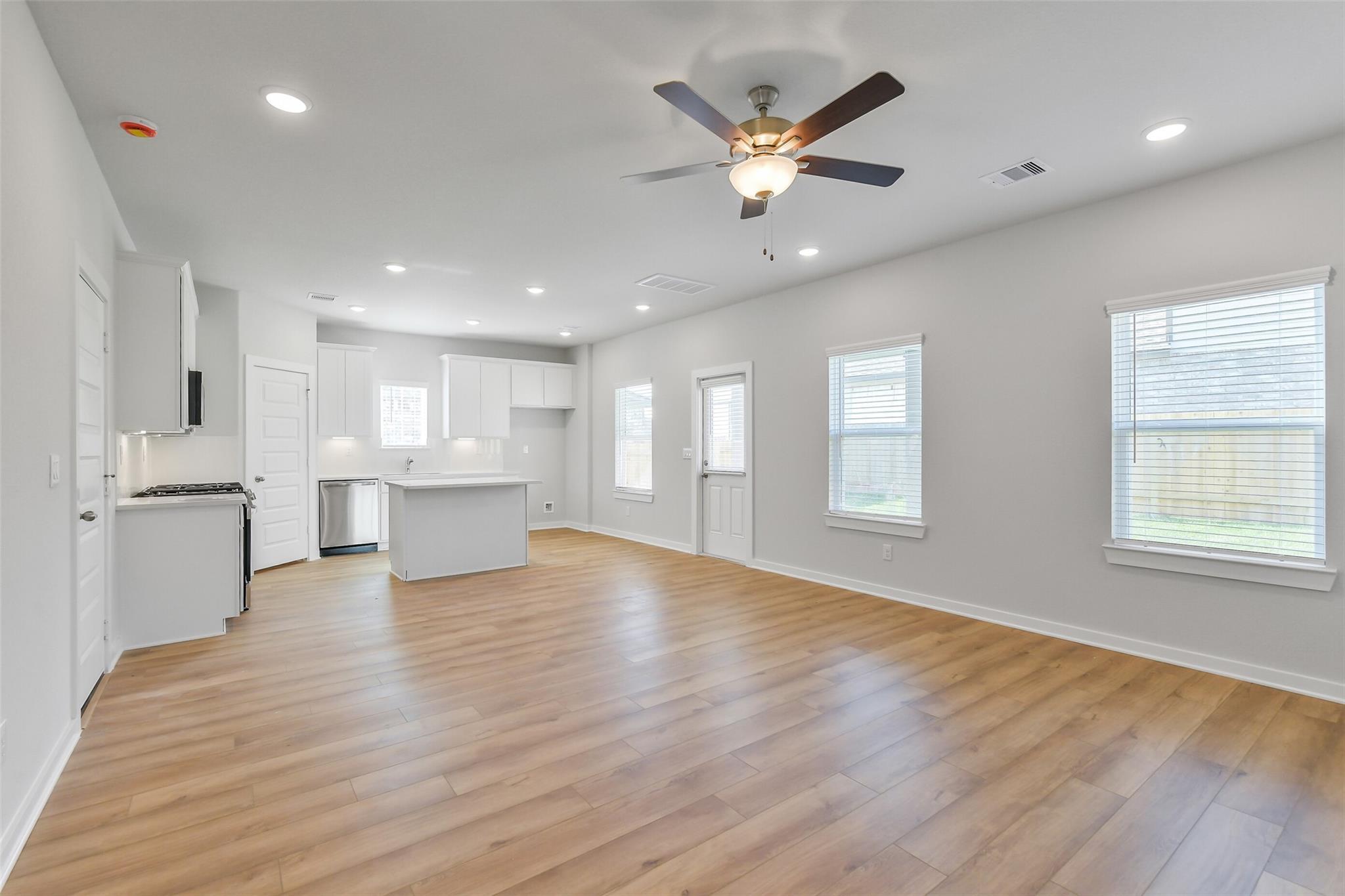 Bright open kitchen with white cabinets, center island, and hardwood floors in Davidson Homes The Trinity F, Magnolia, Texas