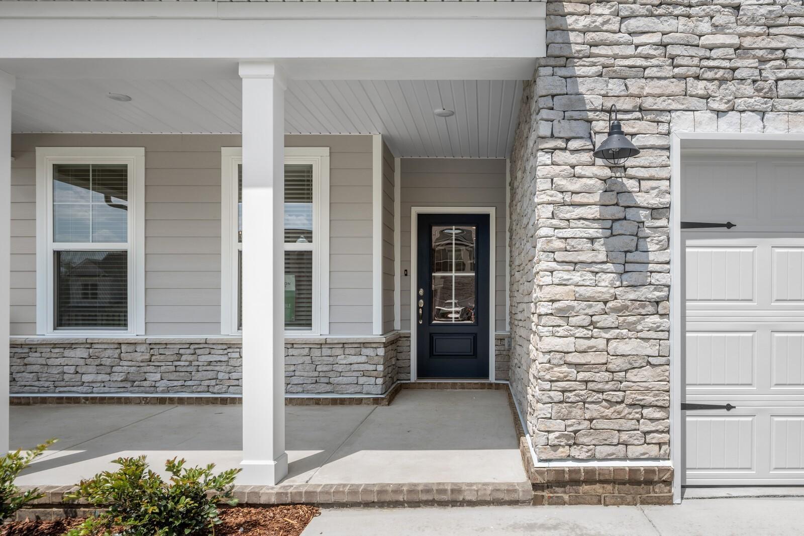Covered front porch with stone facade and dark blue door at The Willow floor plan in Woods Crossing, Gallatin, Tennessee.