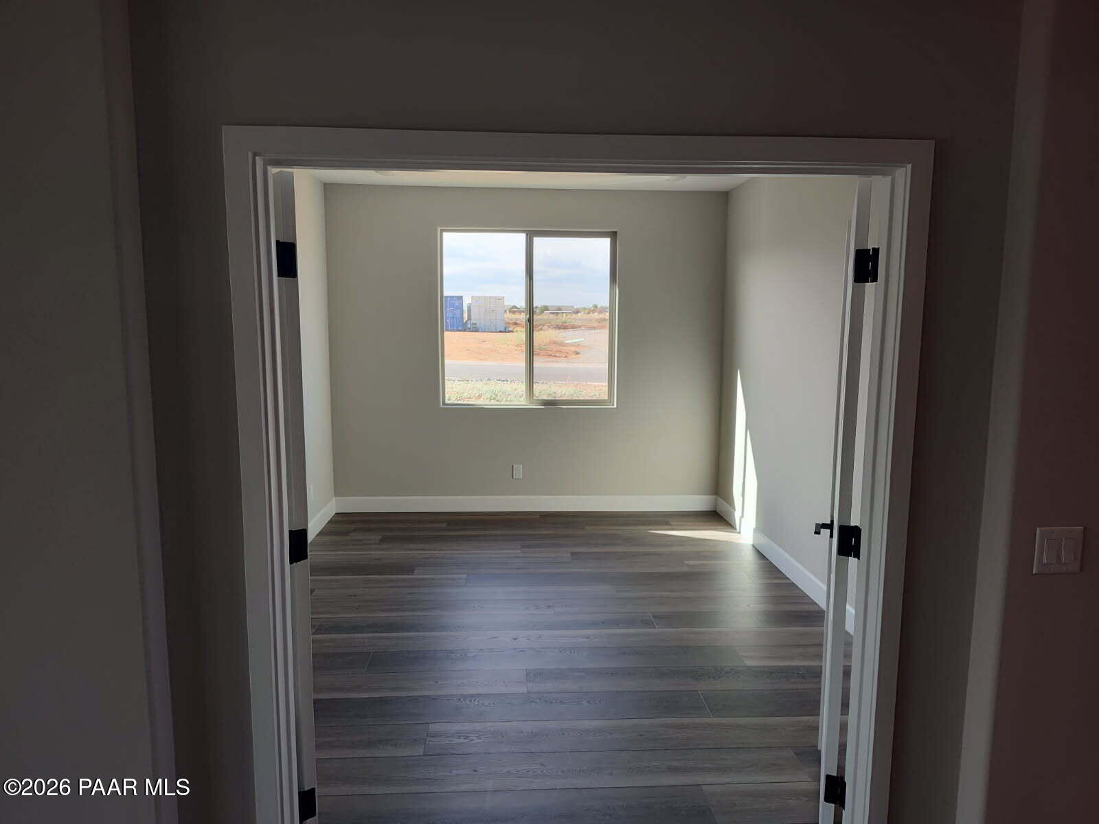 Bright secondary bedroom with neutral gray walls, luxury vinyl plank flooring, and large window to desert view in The Harmony C, Prescott Valley, AZ