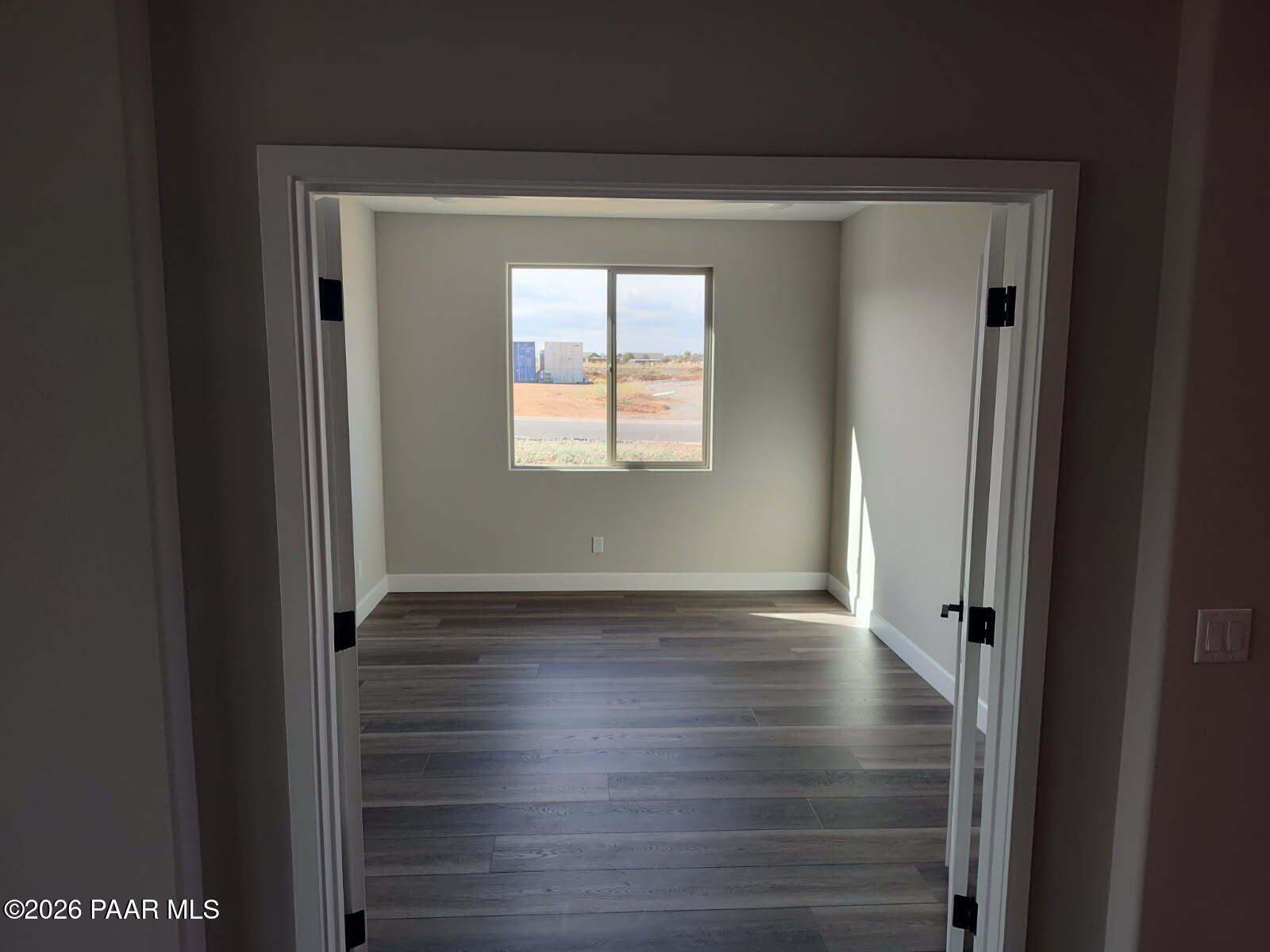 Bright secondary bedroom with neutral gray walls, luxury vinyl plank flooring, and large window to desert view in The Harmony C, Prescott Valley, AZ