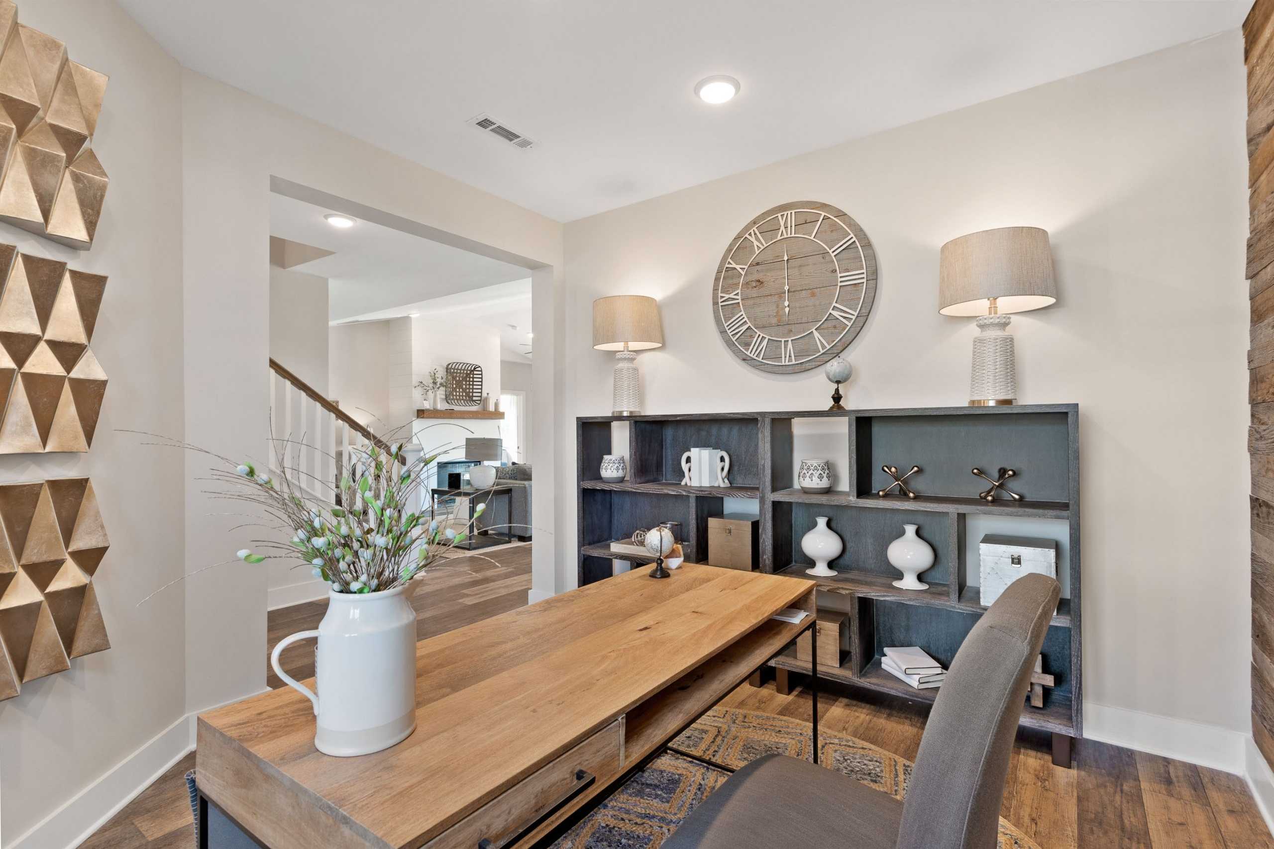 Modern home office at Rivers Edge in Murfreesboro TN by Davidson Homes with wooden desk, gray bookshelves, wall clock, and gold art