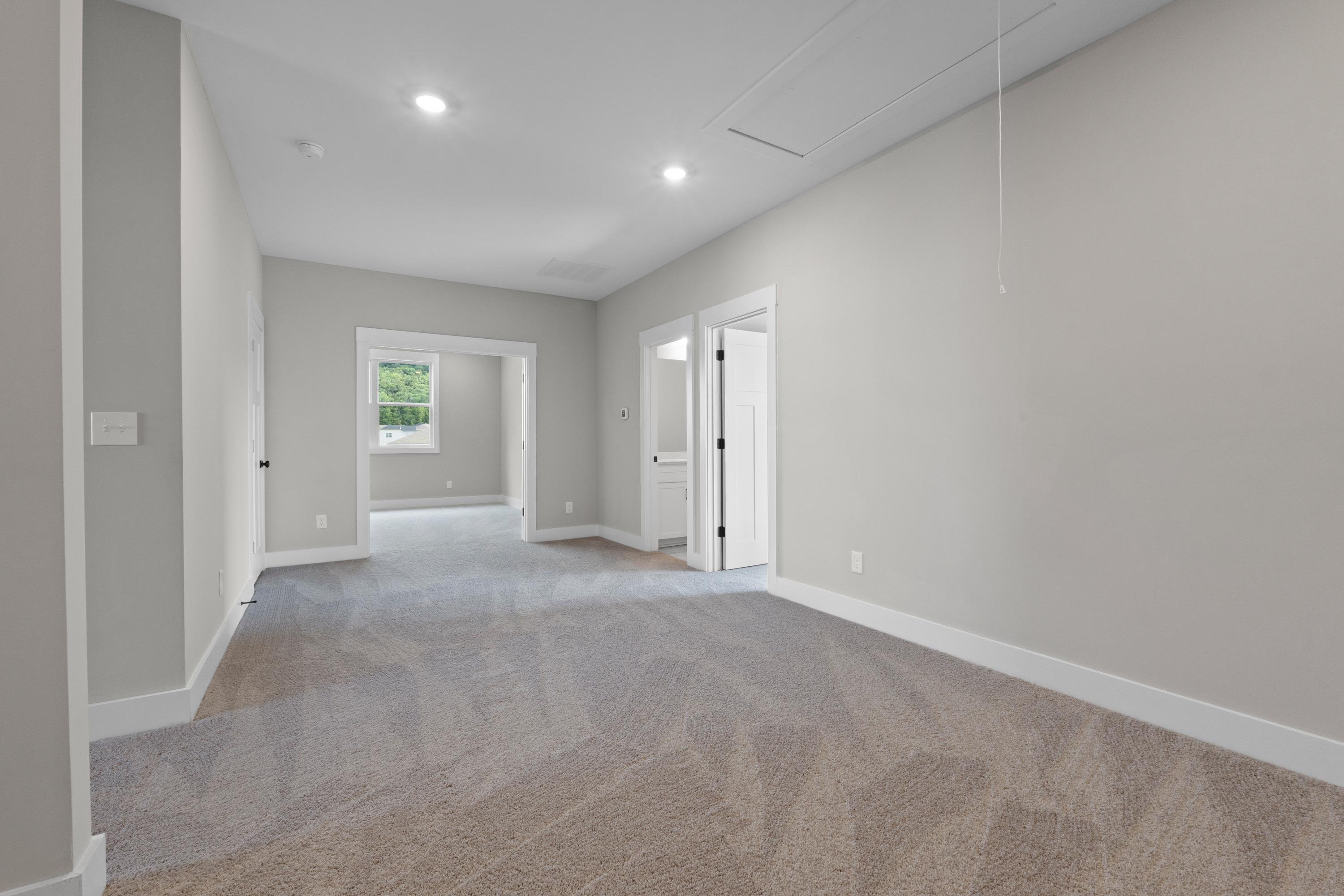 Spacious main floor hallway in The Oxford B home with neutral beige walls, gray carpet, white doors, and natural window light