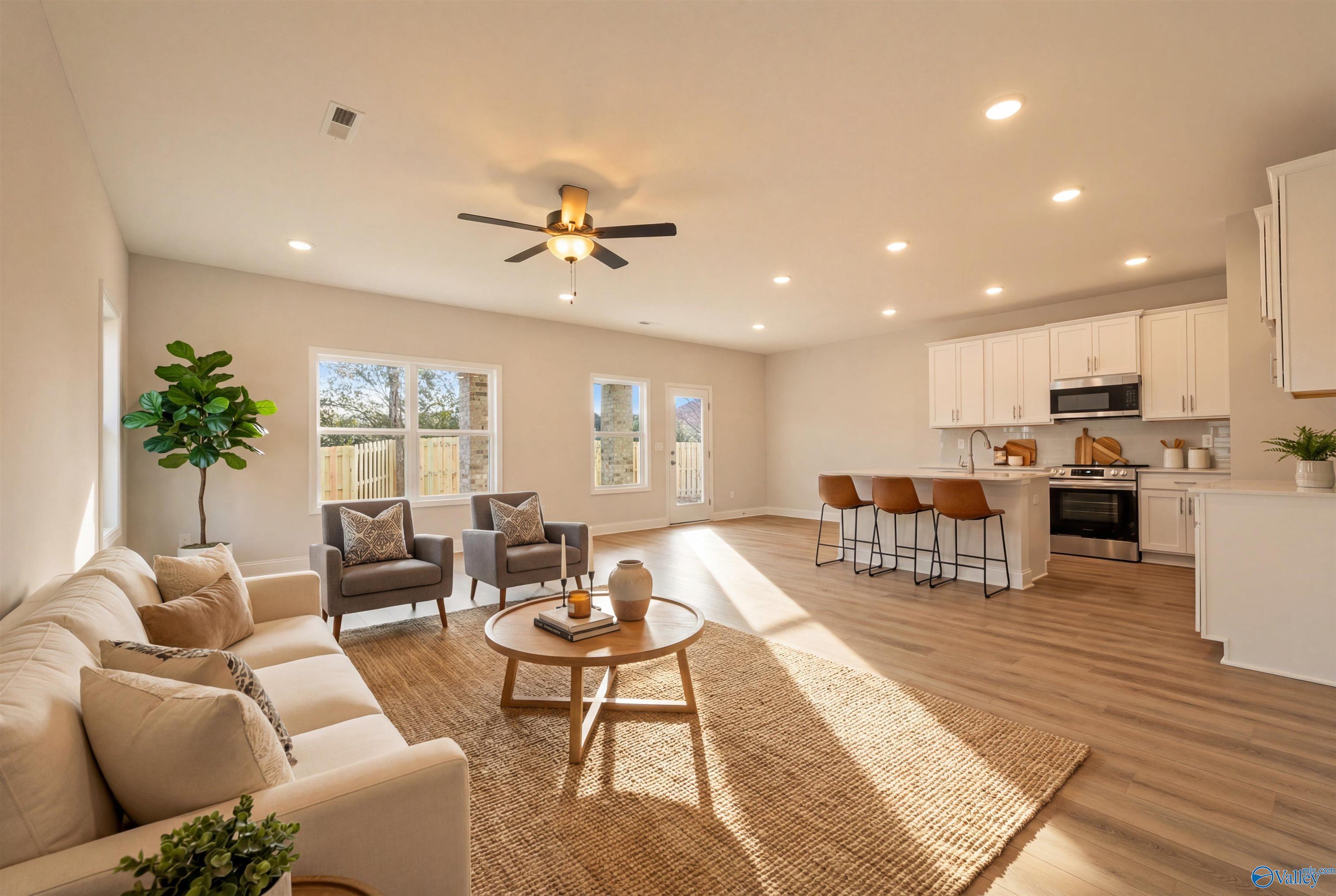 Bright open-concept living room with white sofa, armchairs, ceiling fan, and adjacent white kitchen island in Davidson Homes The Camden, Huntsville, Alabama