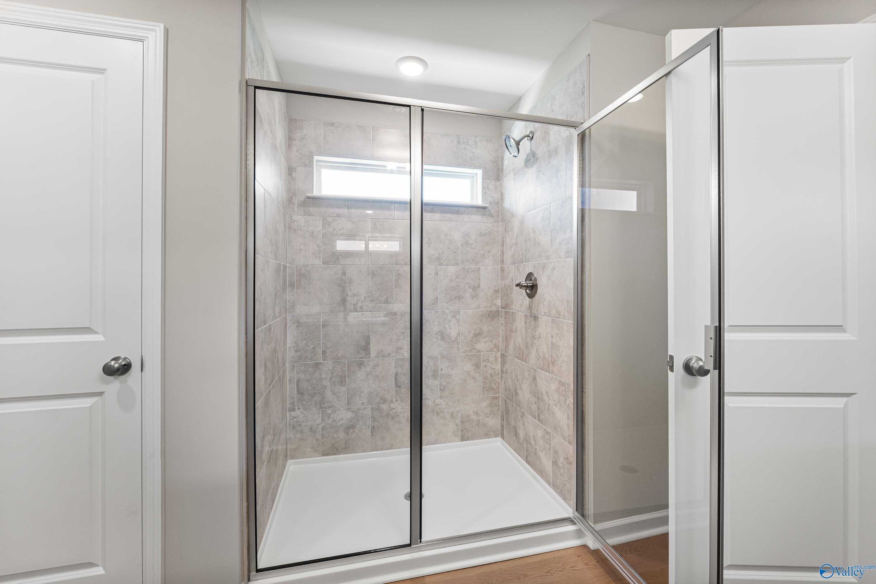 Frameless glass walk-in shower with beige tile walls and white pan in master bath, Davidson Homes The Charm, Huntsville AL