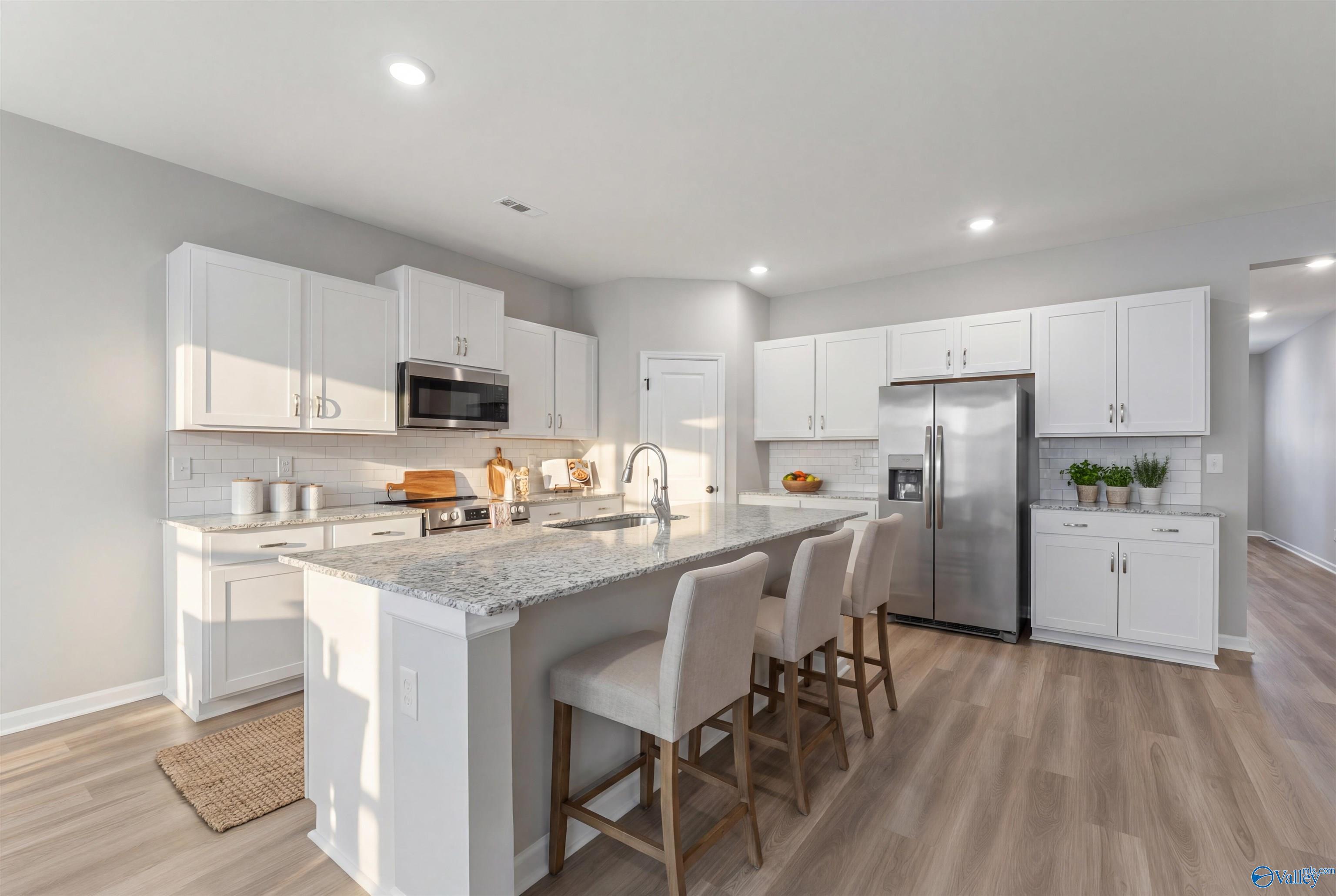 Modern white kitchen with granite island, stainless steel appliances, and bar stools in Davidson Homes The Phoenix, Fayetteville, TN