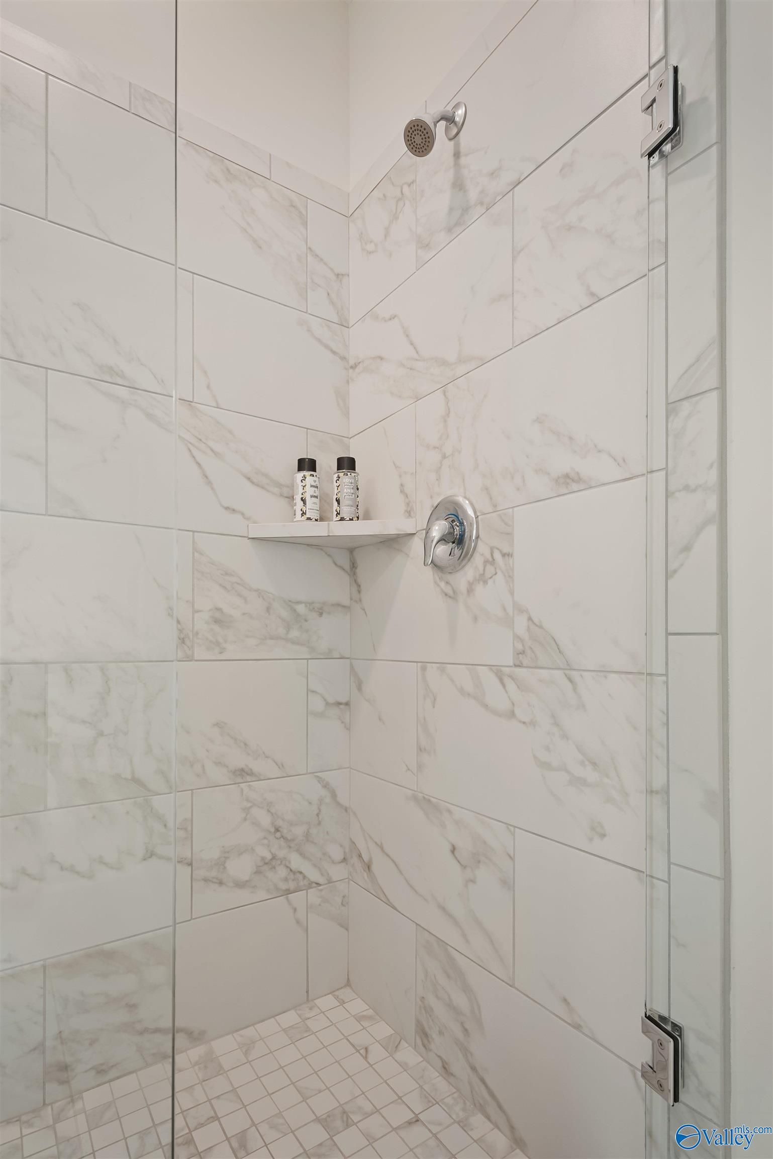 Frameless glass shower with white subway tile walls, rainfall head, and niche shelf in master bath of Davidson Homes The Everett, New Market, Alabama