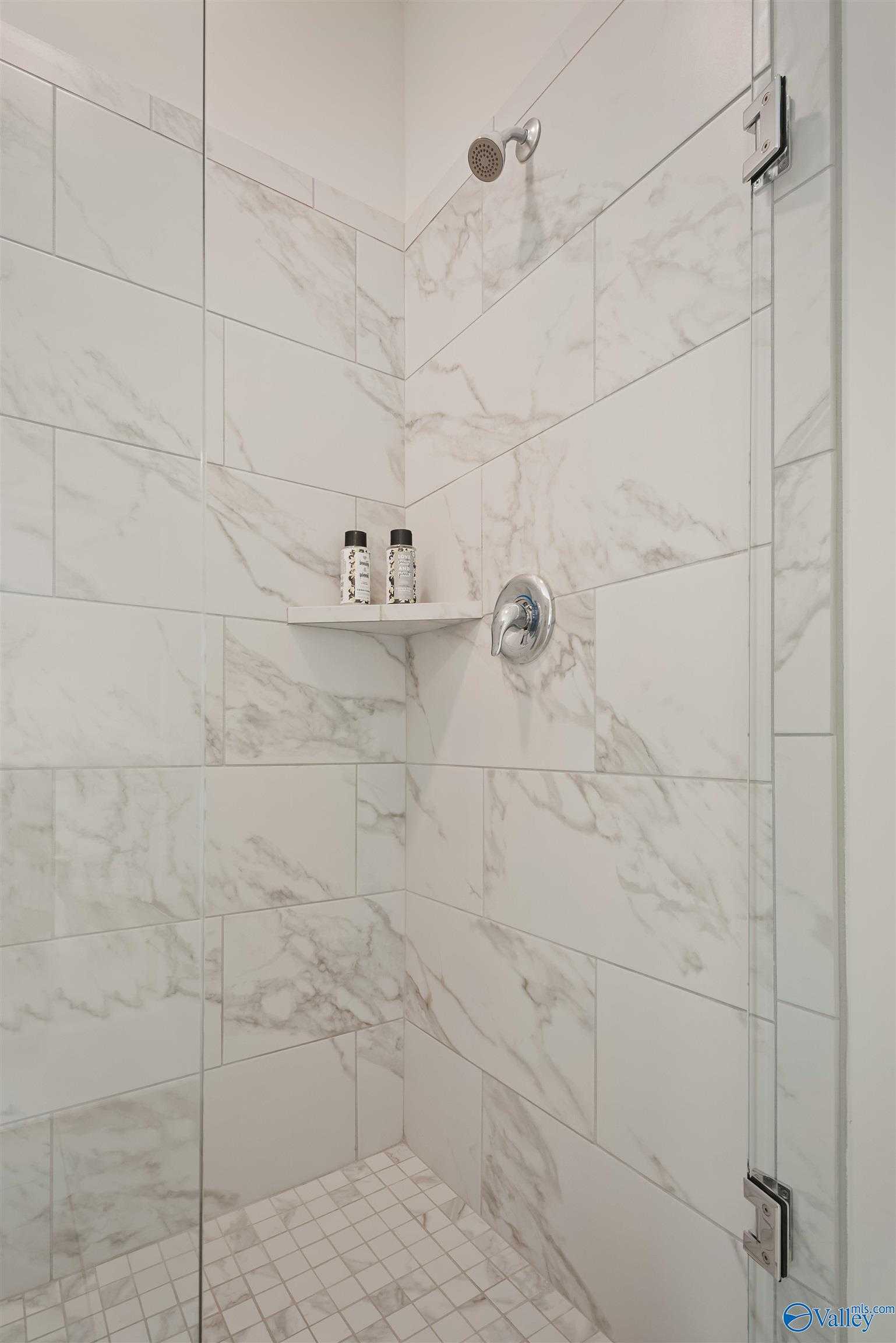 Frameless glass shower with white subway tile walls, rainfall head, and niche shelf in master bath of Davidson Homes The Everett, New Market, Alabama
