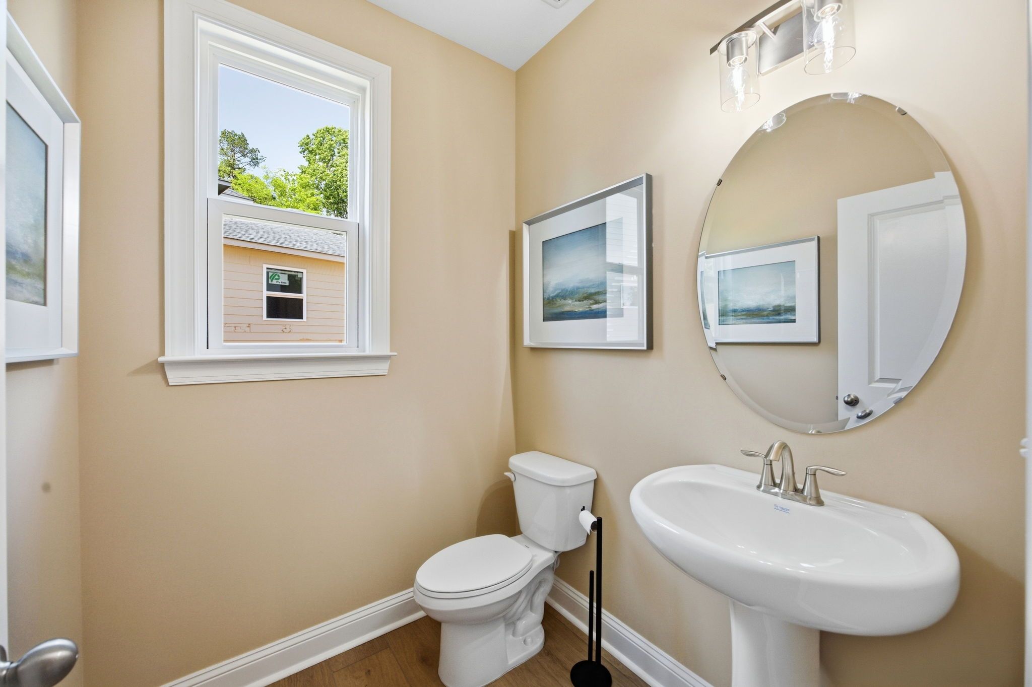 Cozy powder room at Enclave at Belmont in NC by Davidson Homes with beige walls, round mirror, white sink, and tree-view window