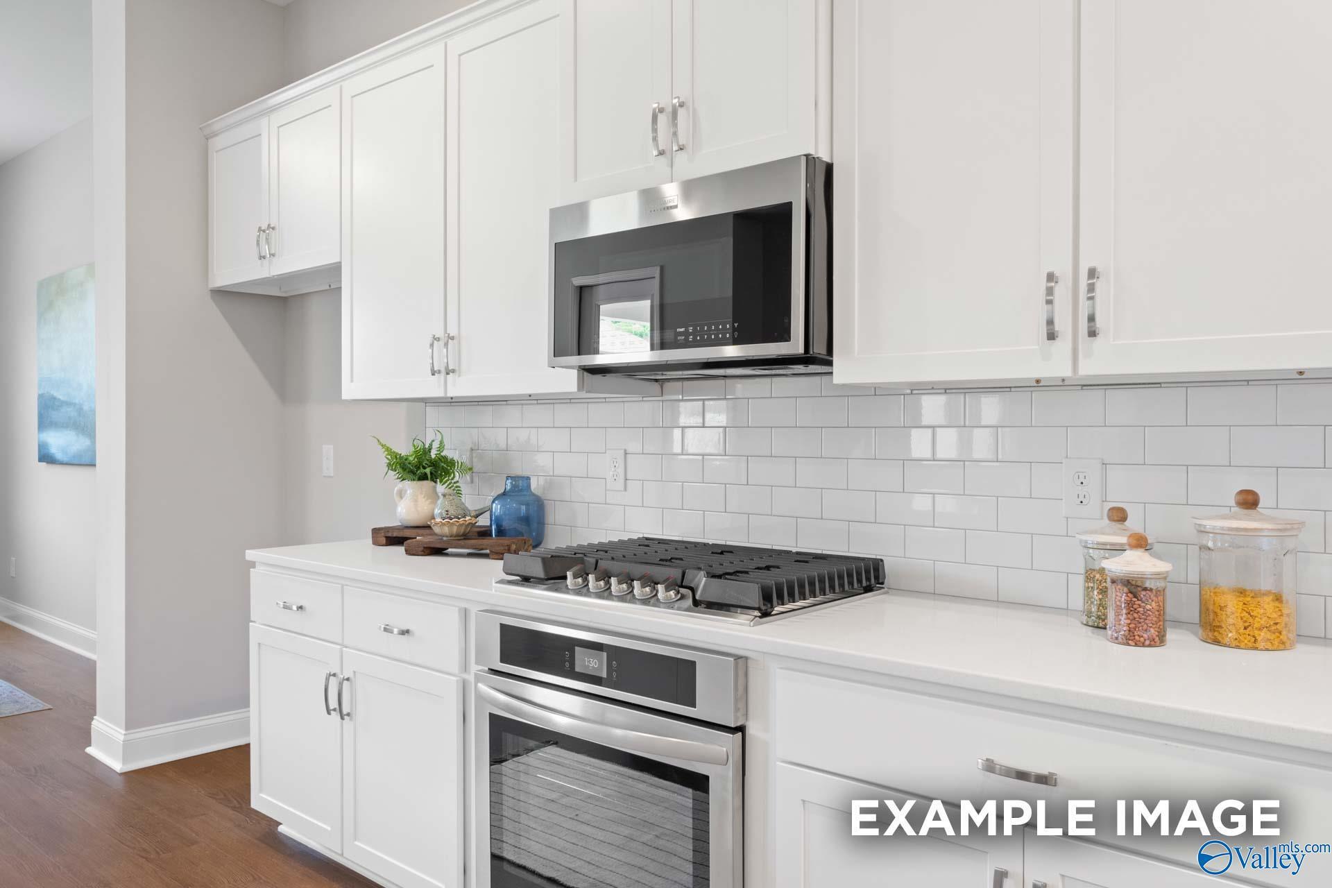 Modern white kitchen with stainless steel gas cooktop, oven, subway tile backsplash in Evermore Homes The Haven E, Owens Cross Roads, AL