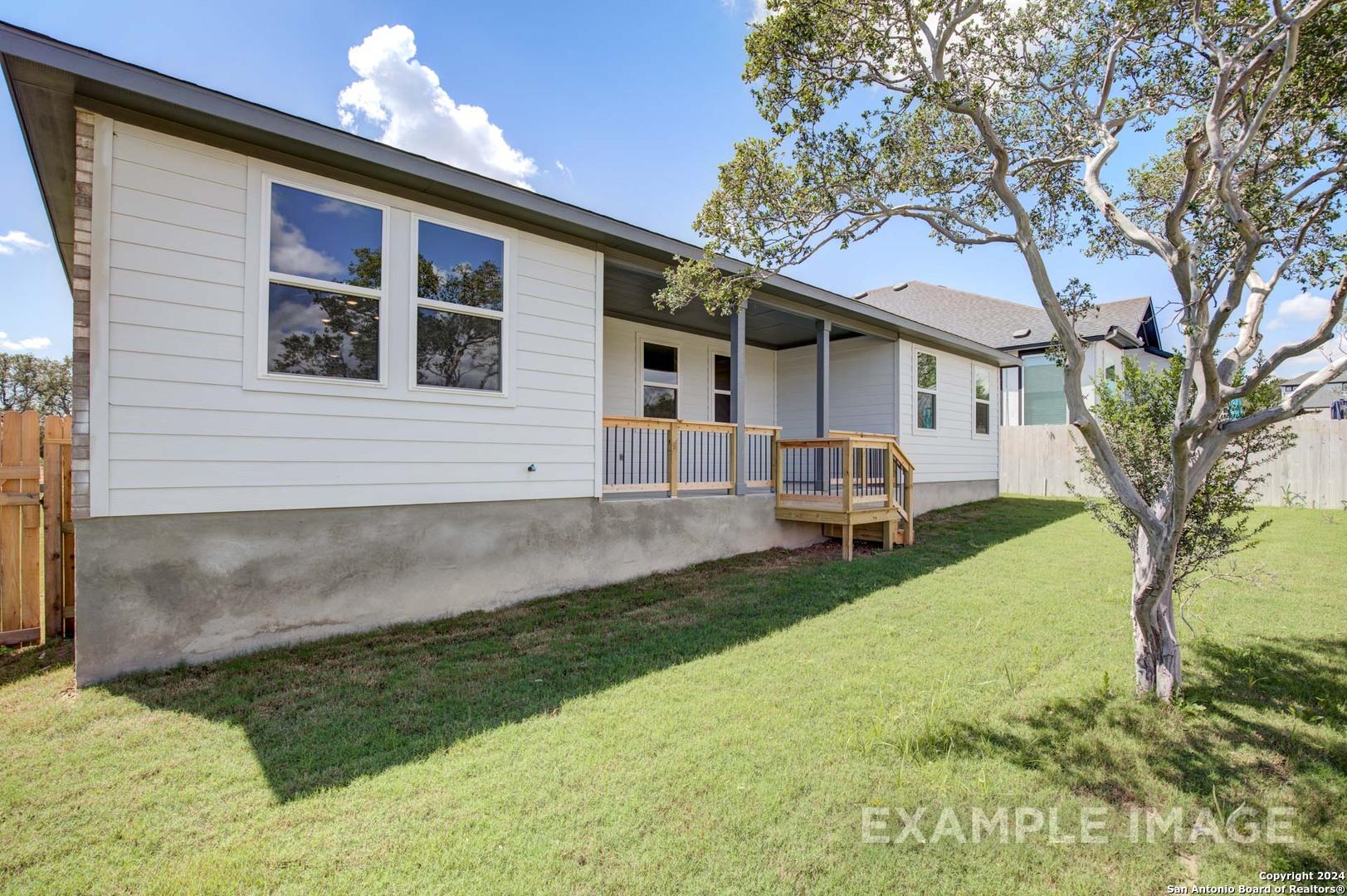 Exterior of The Rockford G single-story home with covered patio, wooden deck, green lawn, and oak tree in Ladera, San Antonio, Texas
