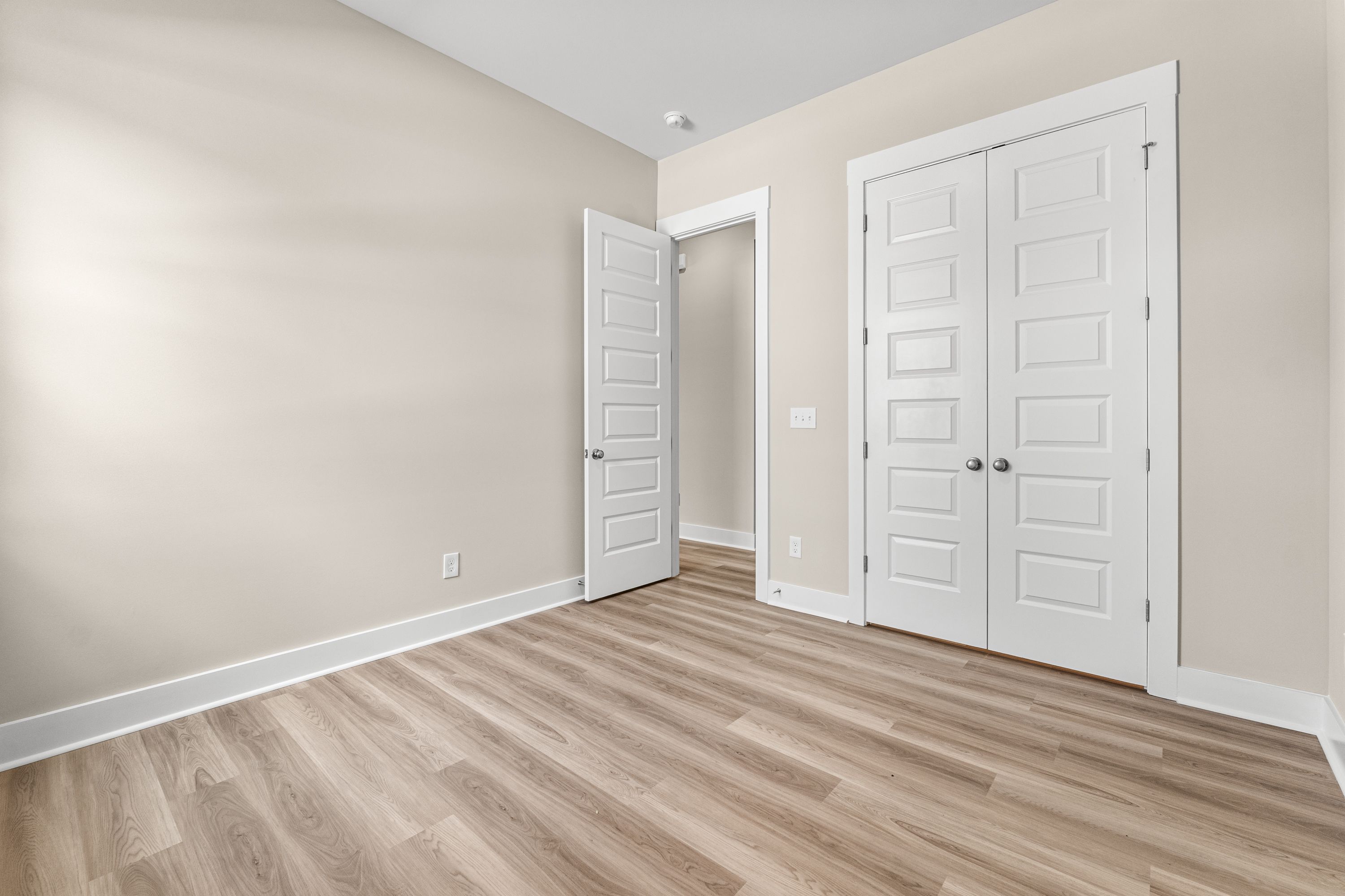 Spacious master suite in The Oxford A home with beige walls, light hardwood floors, and white double doors