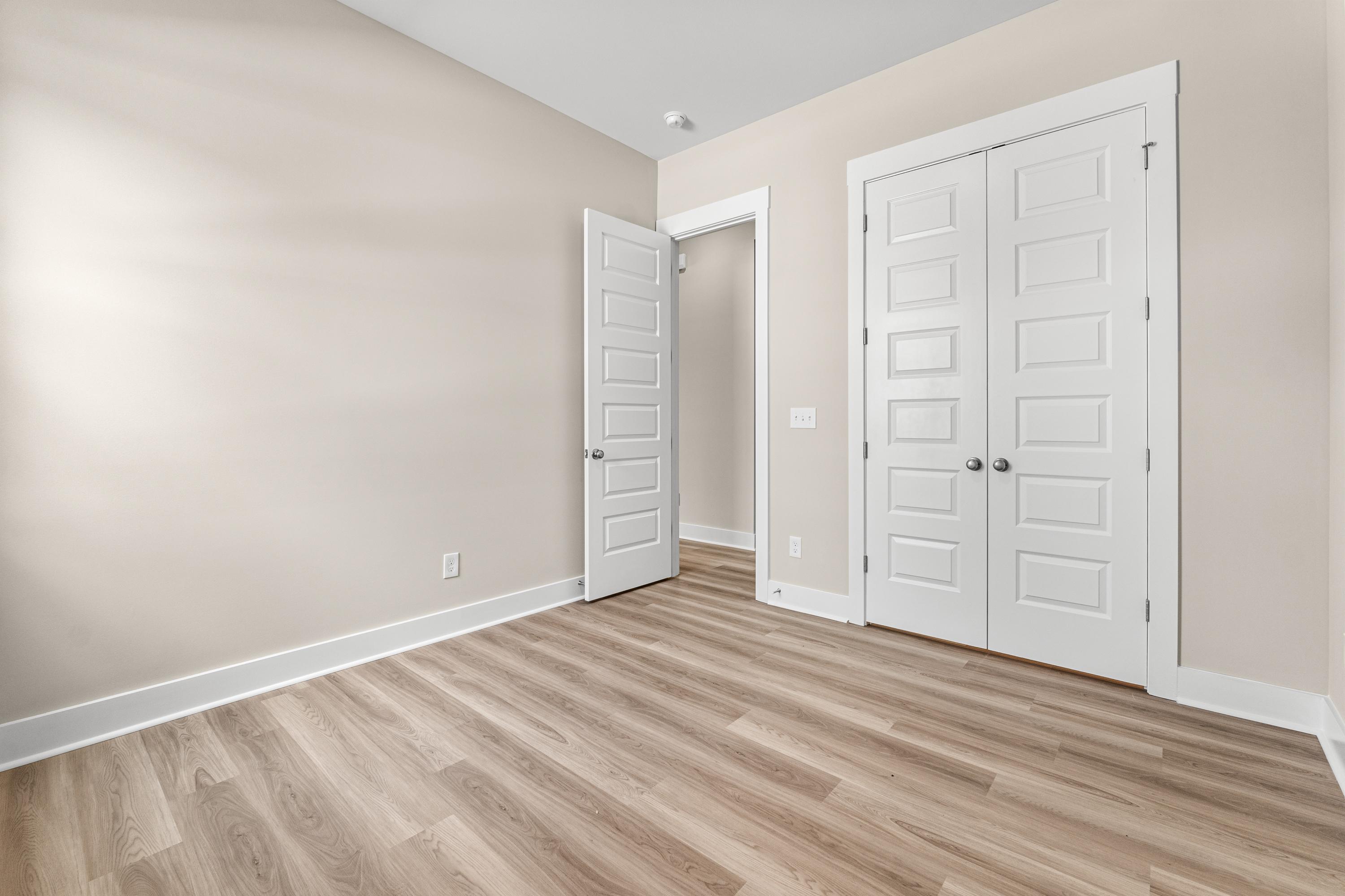 Spacious master suite in The Oxford A home with beige walls, light hardwood floors, and white double doors