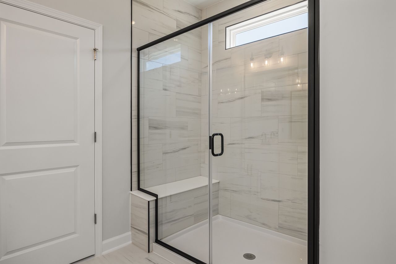 Modern walk-in shower with marble-look tile and black trim in The Birch II master suite by Davidson Homes.