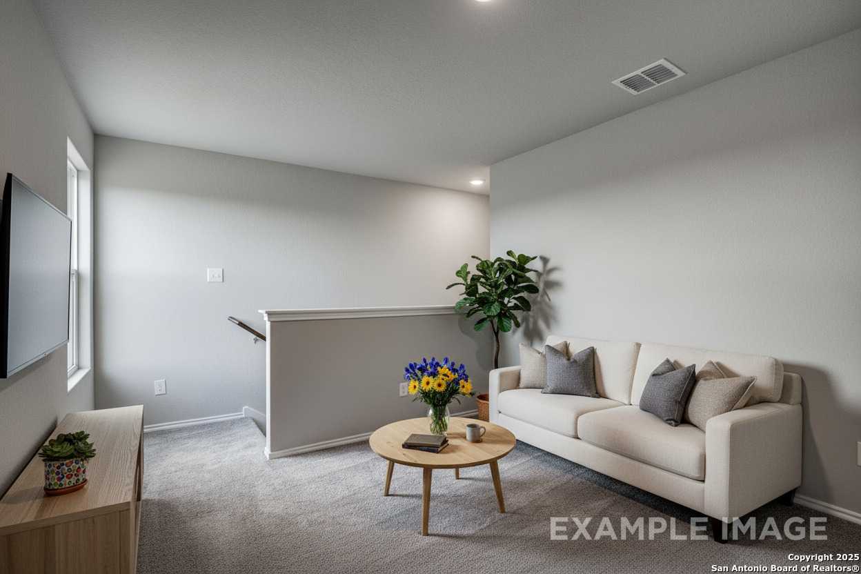 Cozy upstairs loft with wall-mounted TV, beige sofa, coffee table vase, and potted plants in The Blanco C 2-story home, San Antonio