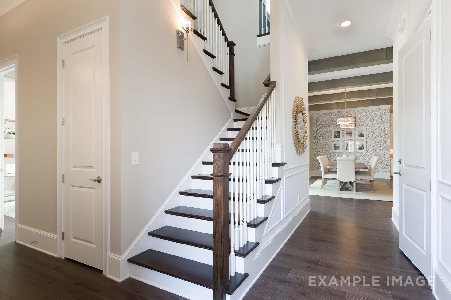 Grand wooden staircase in The Seaside C home design, overlooking open dining area with hardwood floors and neutral walls