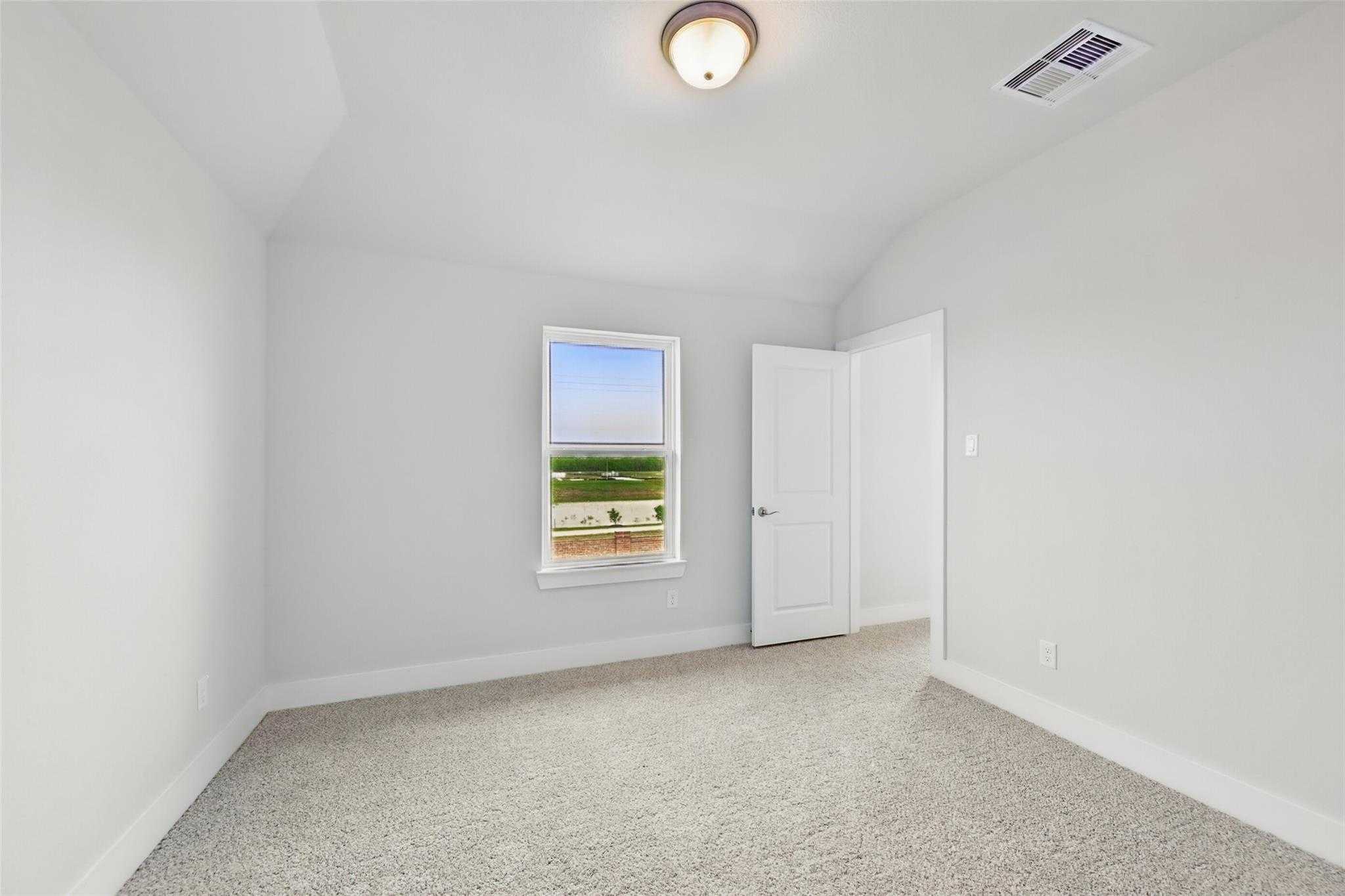 Empty upstairs bedroom with sloped ceiling, window overlooking green landscape, beige carpet and neutral walls in Davidson Homes The Philip A, Lago Mar