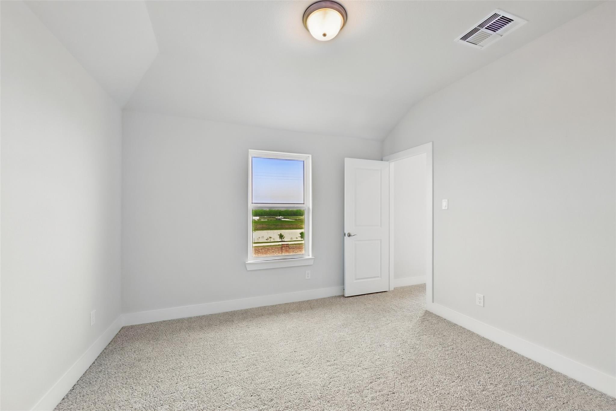 Empty upstairs bedroom with sloped ceiling, window overlooking green landscape, beige carpet and neutral walls in Davidson Homes The Philip A, Lago Mar