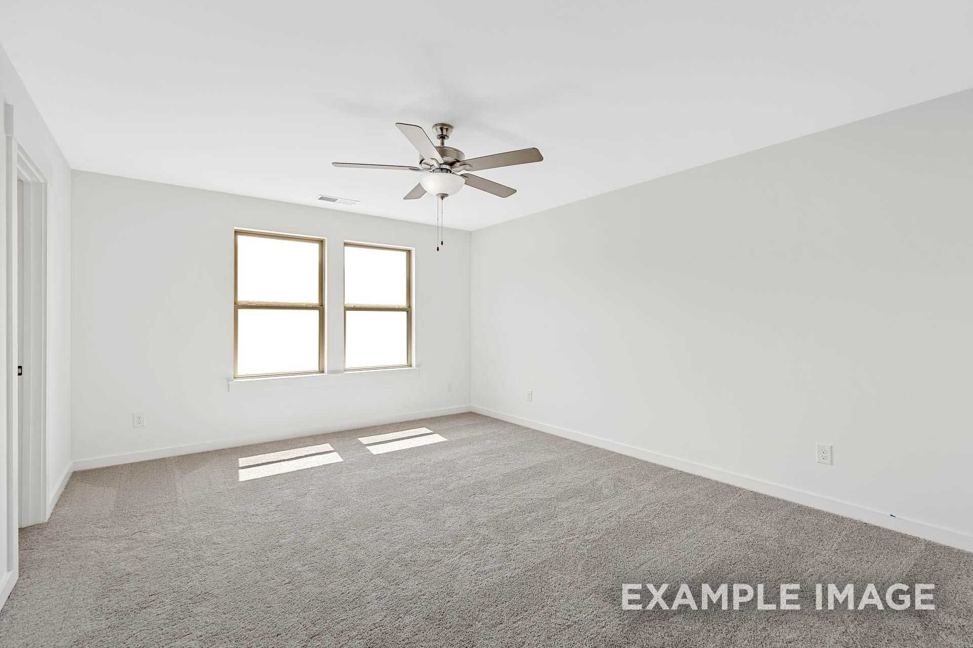 Spacious master bedroom in The Logan B with white walls, double windows, ceiling fan, and carpeted floor